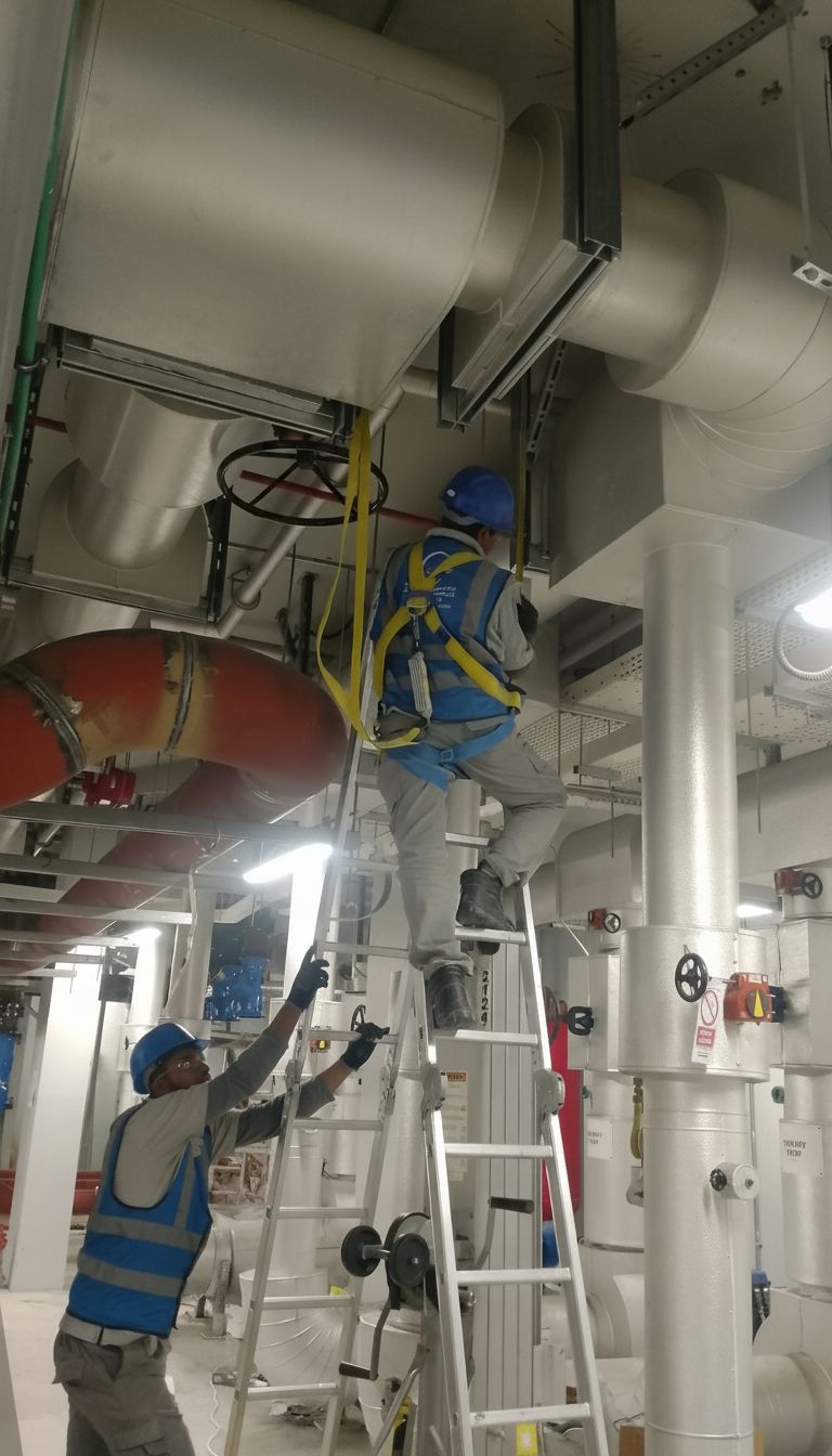 ELCO workers in blue vests and helmets installing HVAC ductwork with safety harness