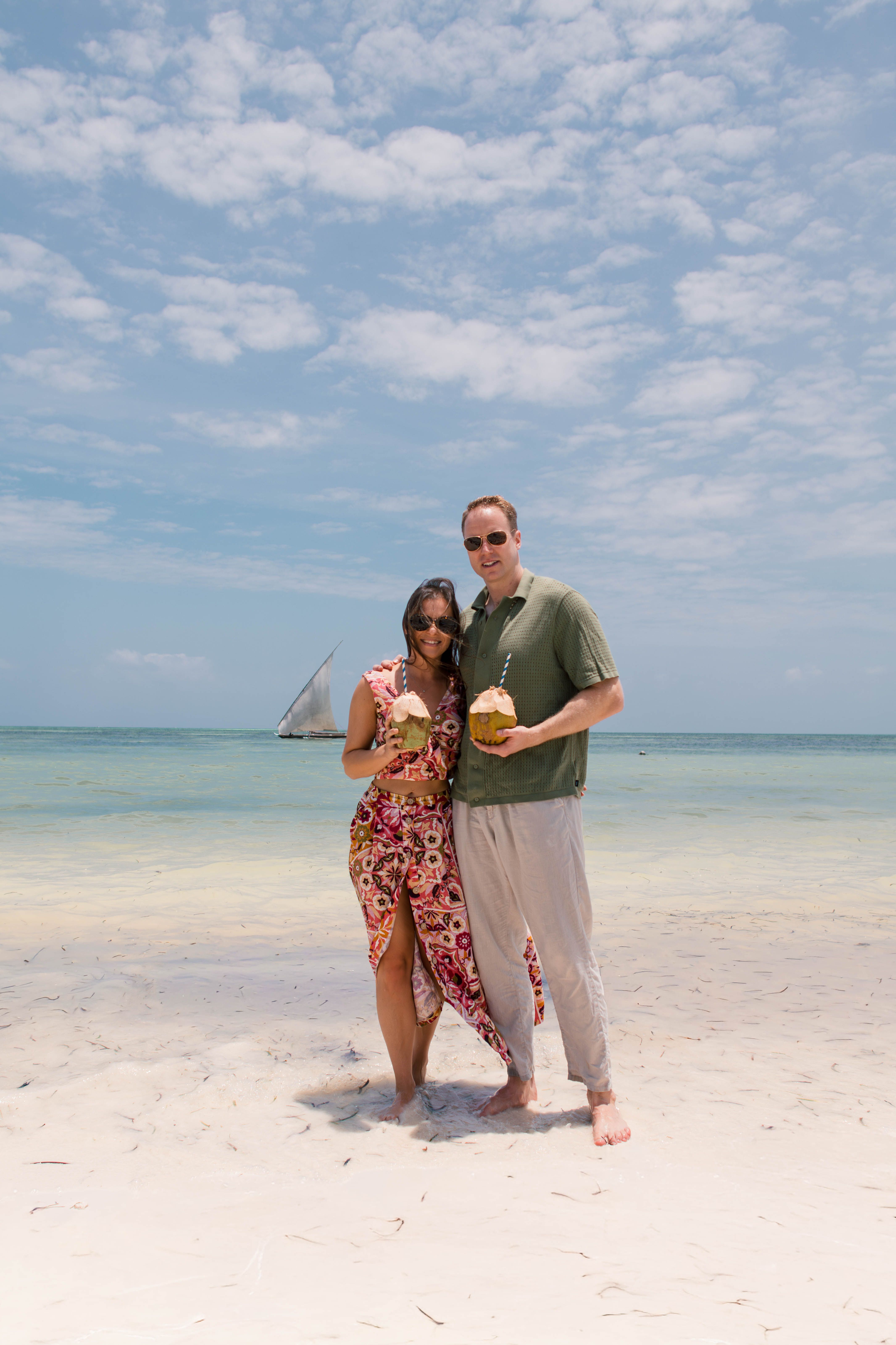 Fun couple with coconuts and sailboat on beach