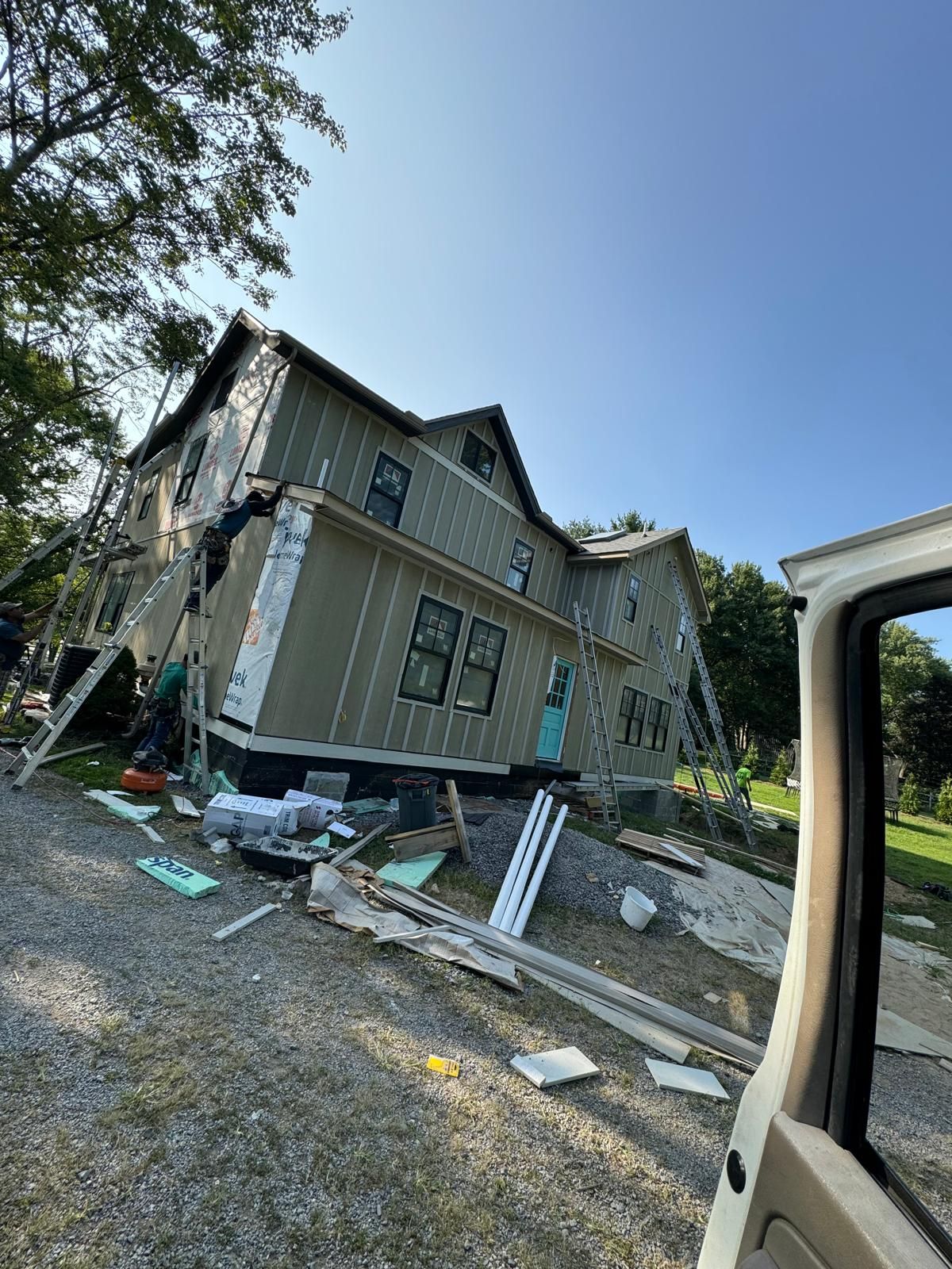 Two-story home with dark siding and construction crew at work