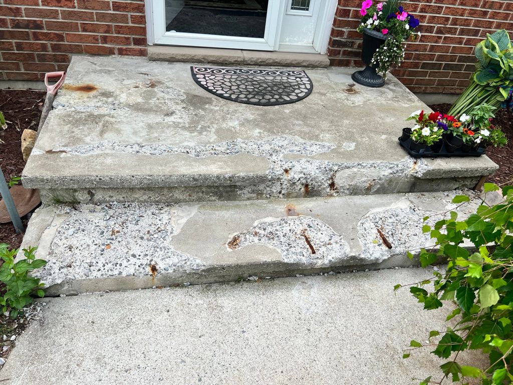 Concrete front porch with two steps showing surface deterioration, exposed aggregate and rust stains before restoration