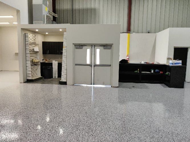 Retail storage and service area with speckled gray seamless floor, double push-bar doors and metal shelving with supplies