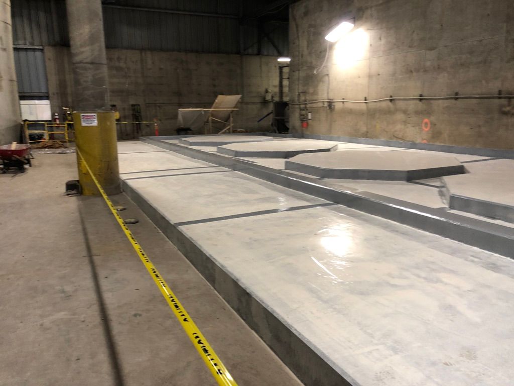 Large water treatment facility interior with raised concrete platforms in rectangular and hexagonal shapes, yellow caution tape and industrial equipment in the background