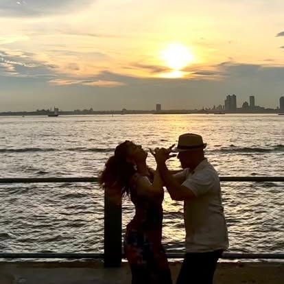 Two people dancing by the waterfront at sunset