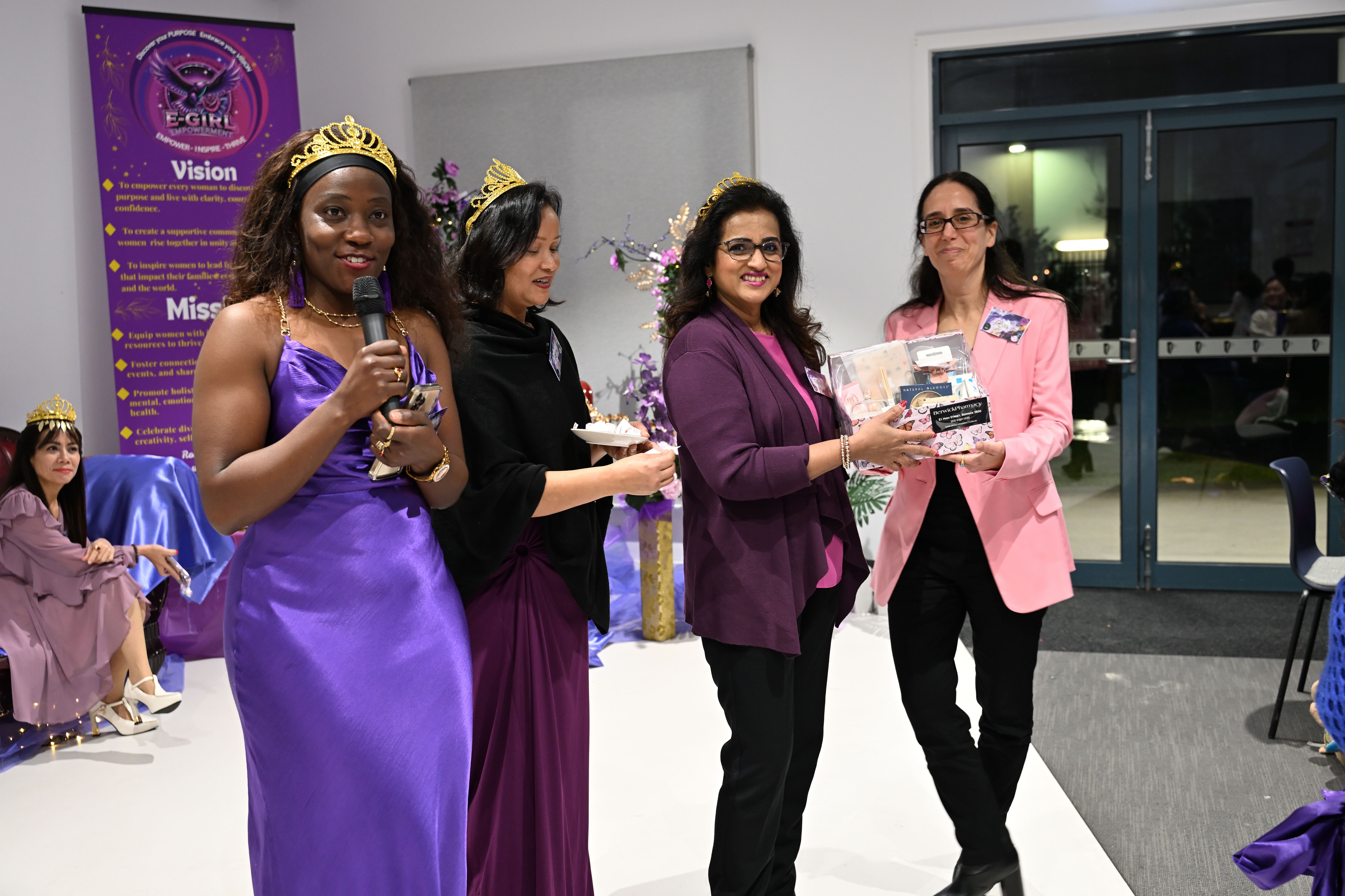 Women in tiaras presenting a gift basket at an E-Girl Empowerment celebration event