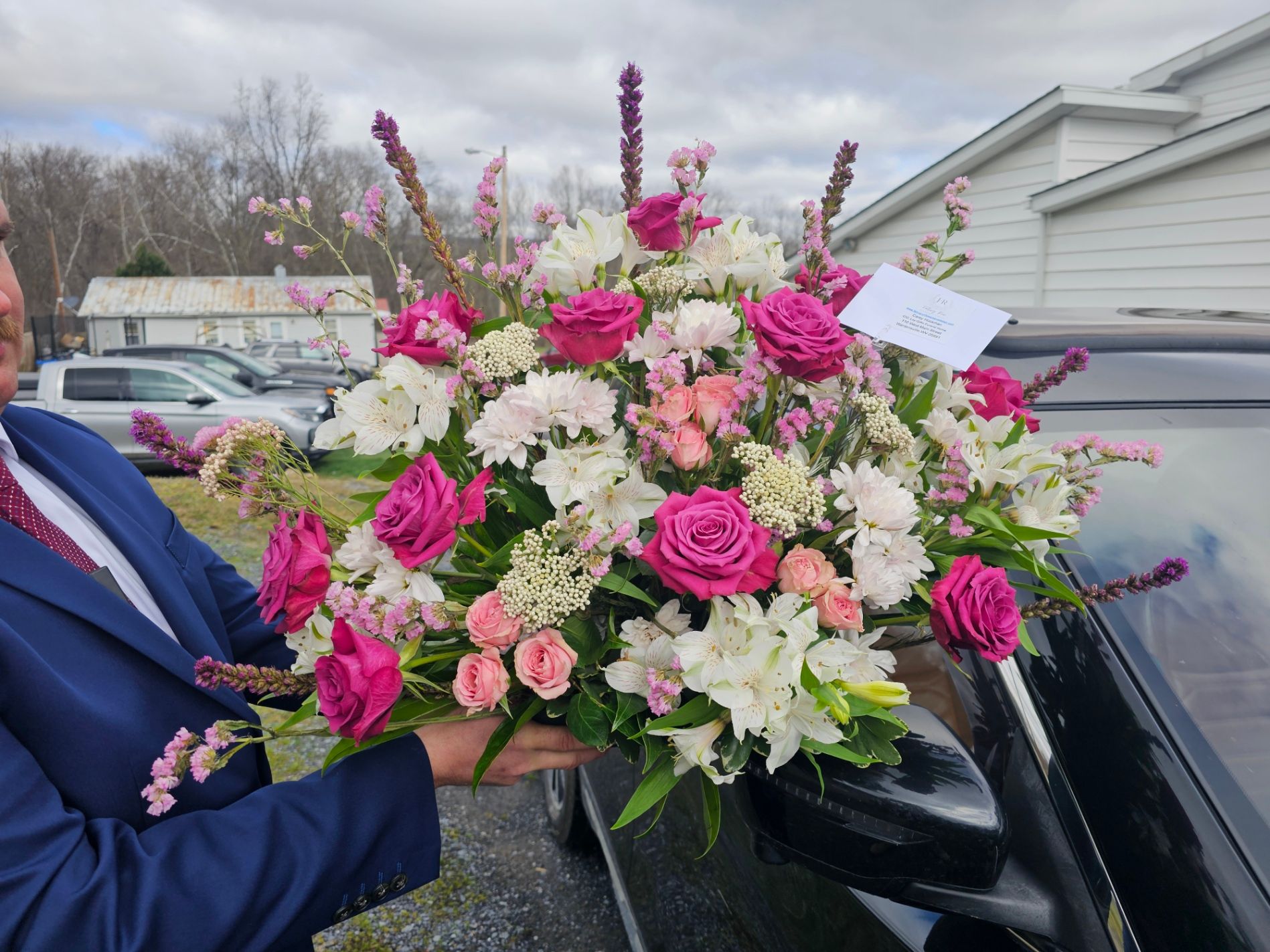 Groomsman holding a vibrant bridal bouquet of pink roses, white lilies, and greenery
