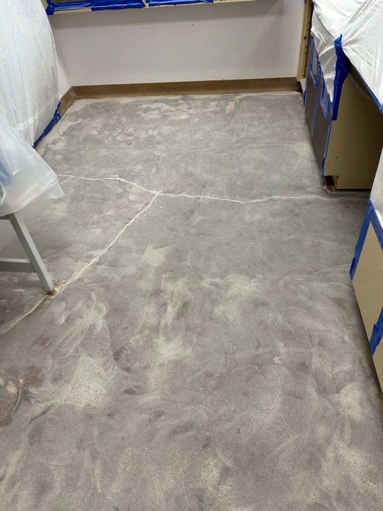 Close-up of a pharmaceutical lab floor with crack repair work completed and fresh filler visible, cabinetry masked with painter's tape alongside