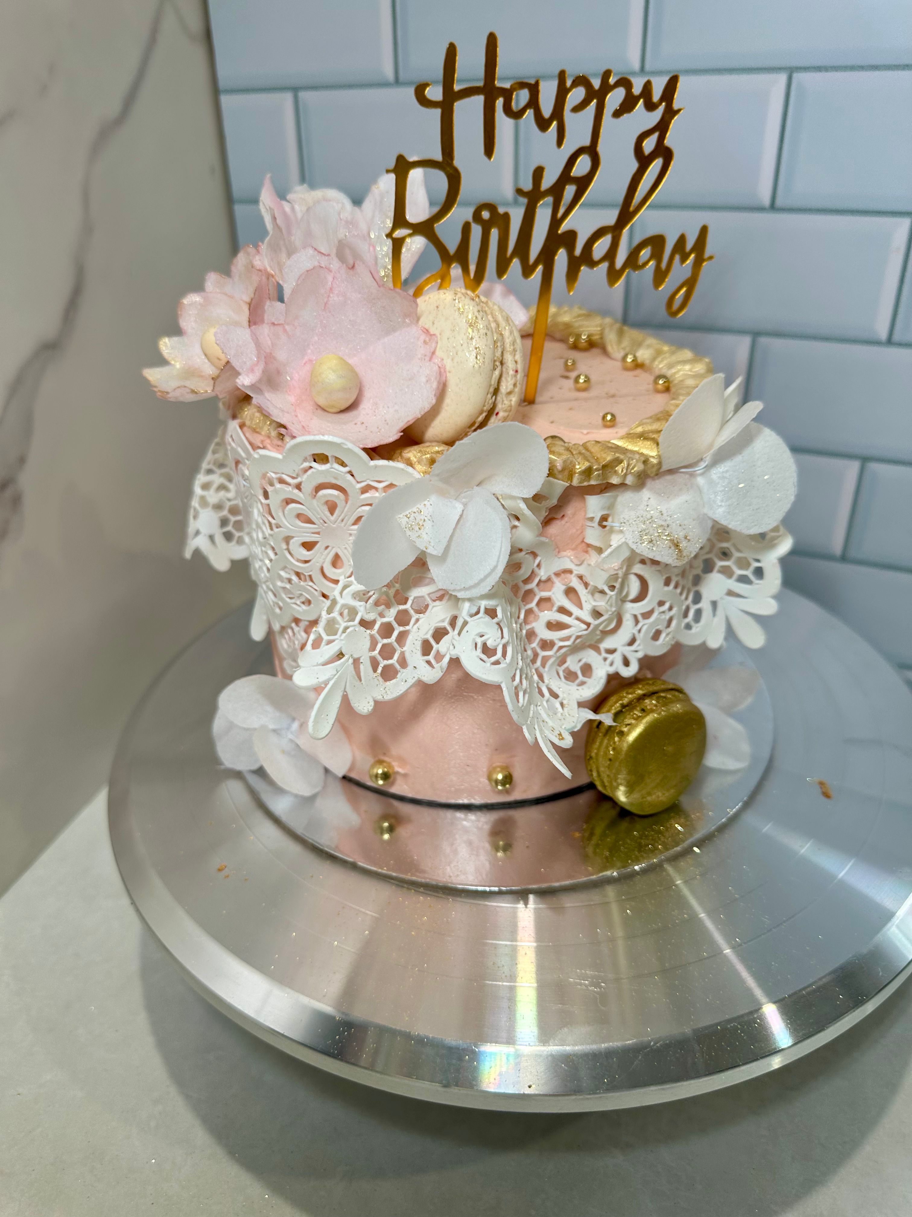 Pink birthday cake with lace wrap, macarons and gold topper