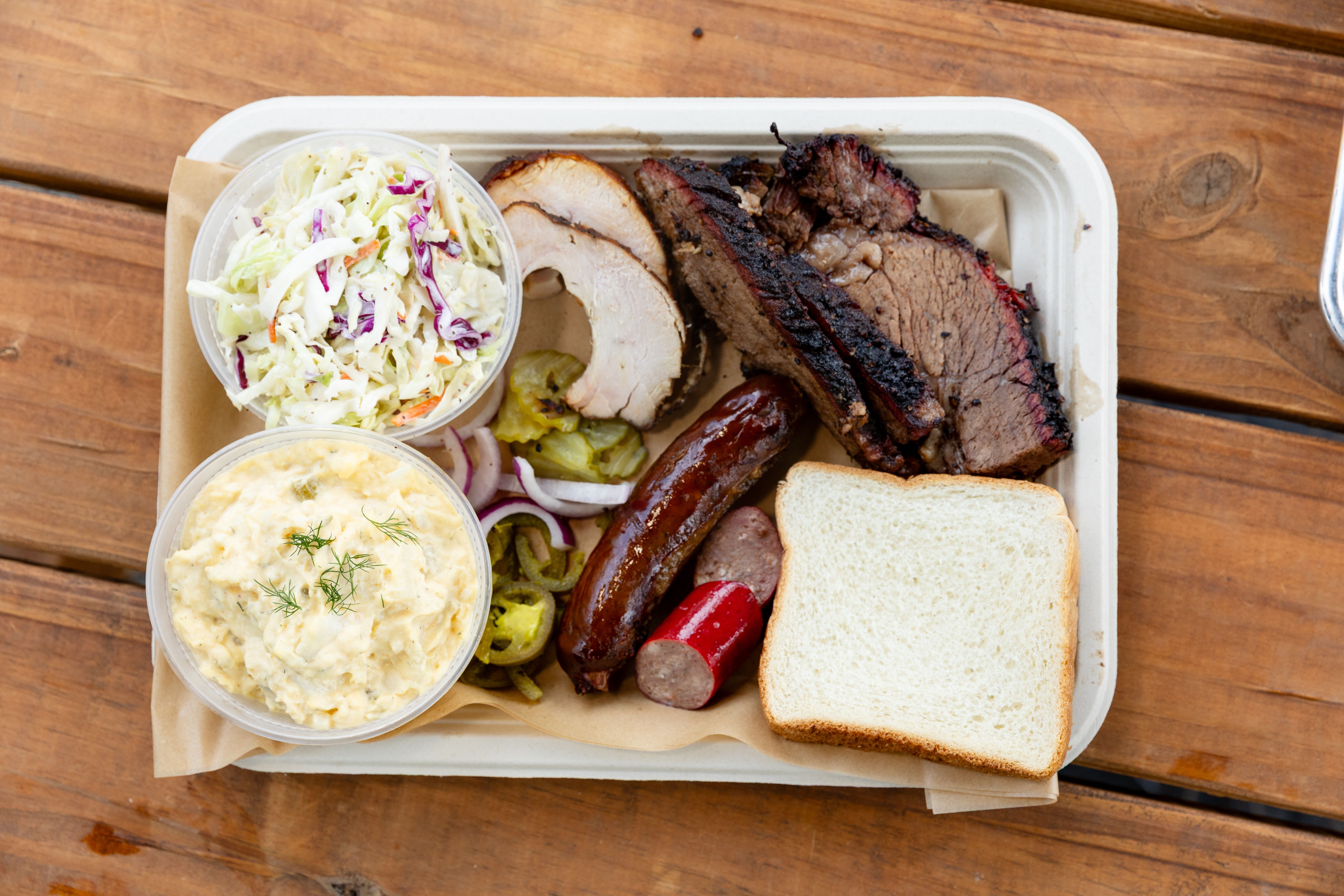 BARK'D BBQ smoked brisket, sausage and sides arranged in a lunch tray