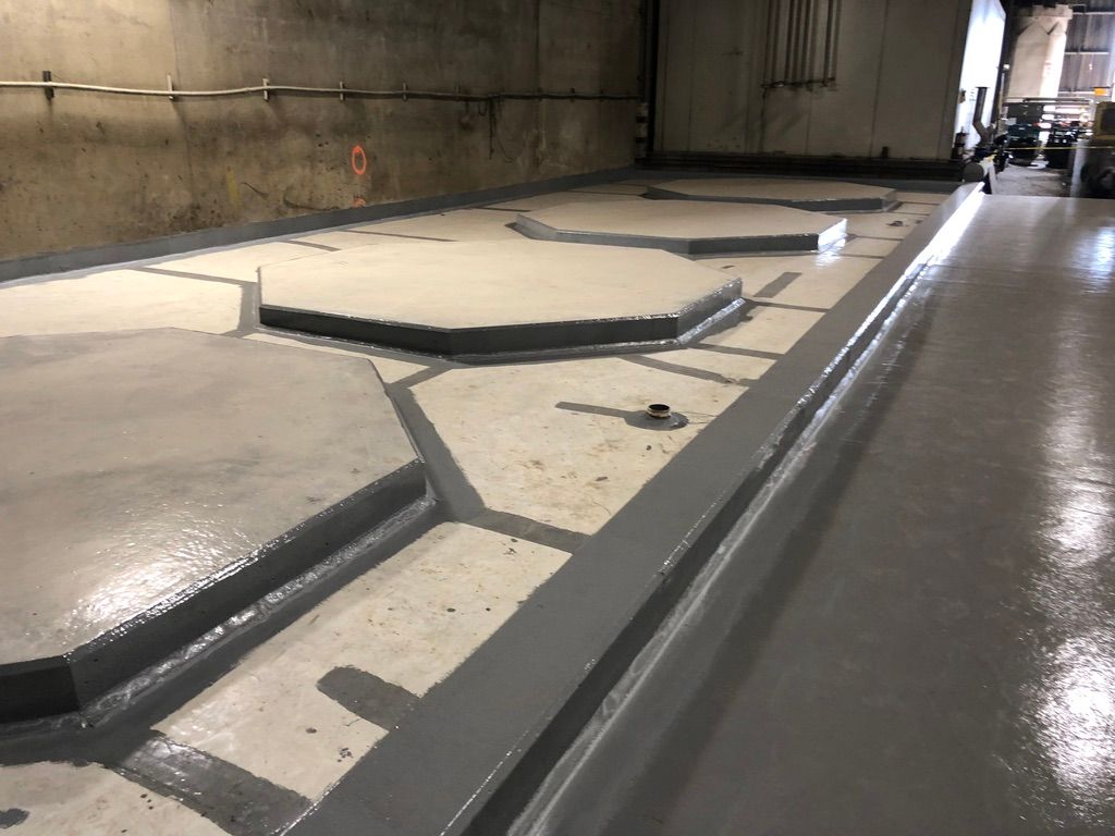 Water treatment facility floor with multiple raised octagonal sumps and containment platforms coated in seamless grey epoxy, pipes protruding from the floor surface