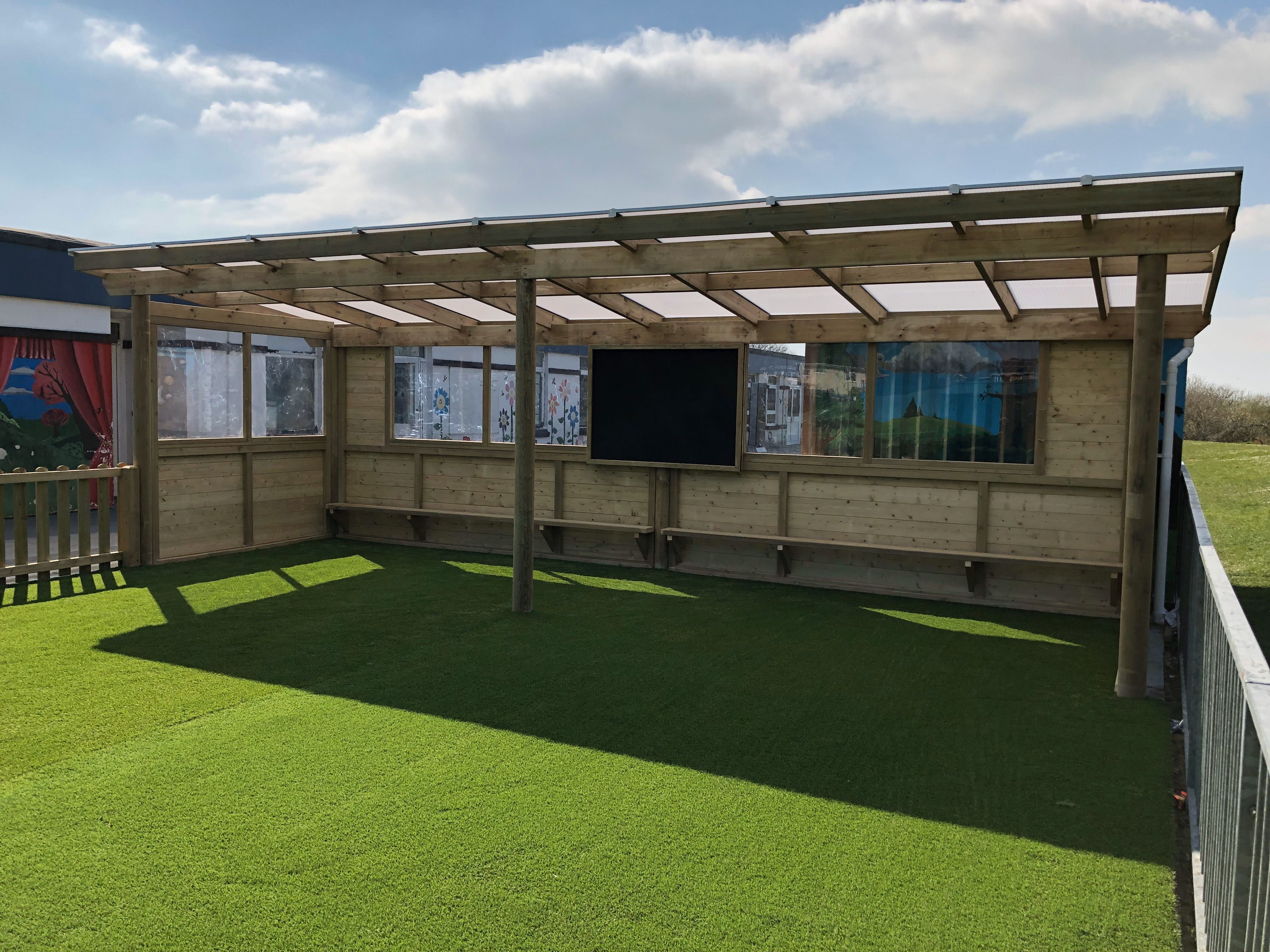 Open-sided outdoor classroom with benches and blackboard wall
