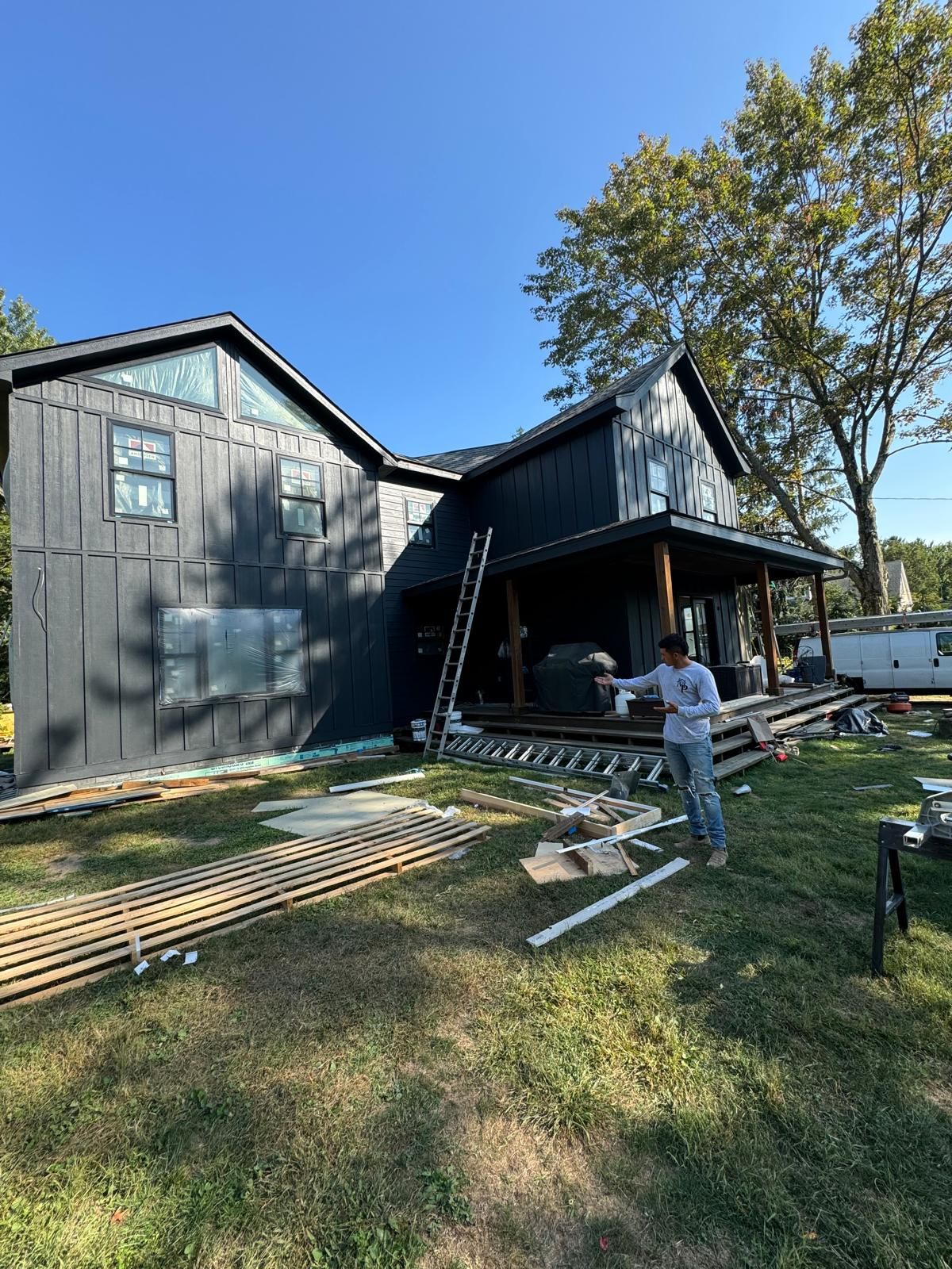 Dark-sided two-story home with construction materials and crew member on site