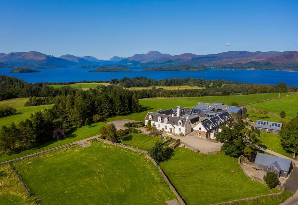 Aerial view of Ardoch Loch Lomond estate — exclusive use corporate venue overlooking Loch Lomond with grey-roofed buildings and mountain backdrop