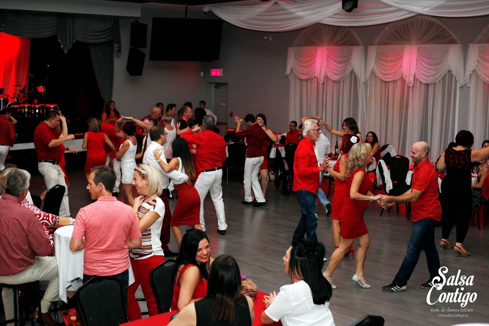 Soirée Salsa Contigo — couples dansant, ambiance festive et chaleureuse avec éclairage rosé et musiciens en arrière-plan