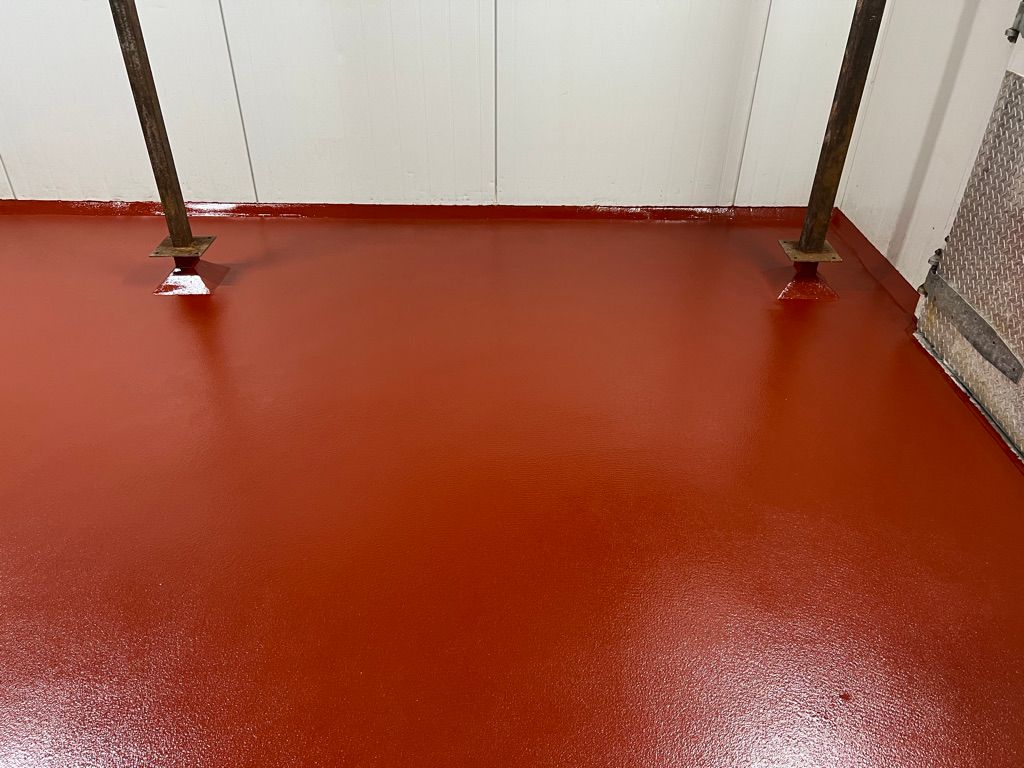 Close-up of seamless red epoxy floor with metal bollards and diamond-plate panel in food facility