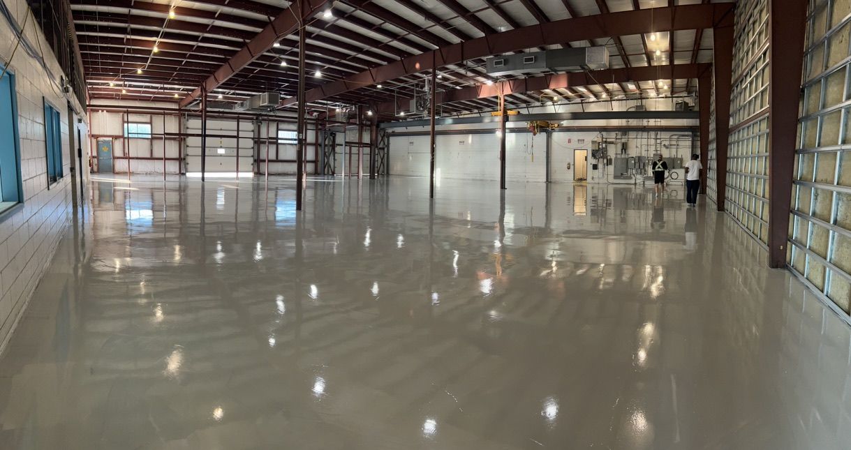 Large empty industrial warehouse with highly reflective polished concrete floor and two workers near electrical panels at far wall