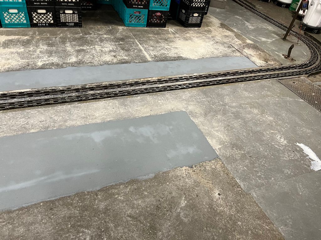 Concrete floor repair with fresh gray cement patches around embedded metal track in food facility