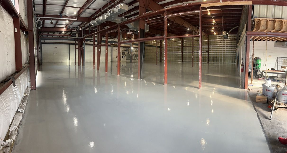 Empty industrial warehouse with polished reflective concrete floor, exposed beams, red metal columns and product containers on right