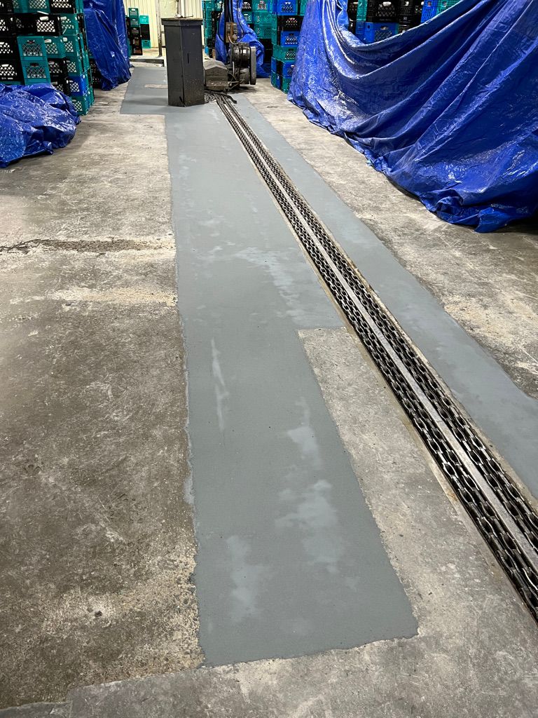 Freshly resurfaced concrete floor with embedded chain track in active food and beverage facility