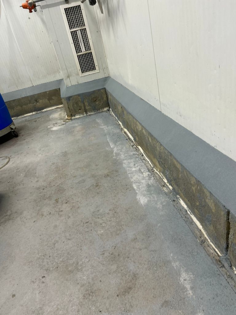 Wall corner with gray cove base strip, blue barrel and vent panel before final surface restoration