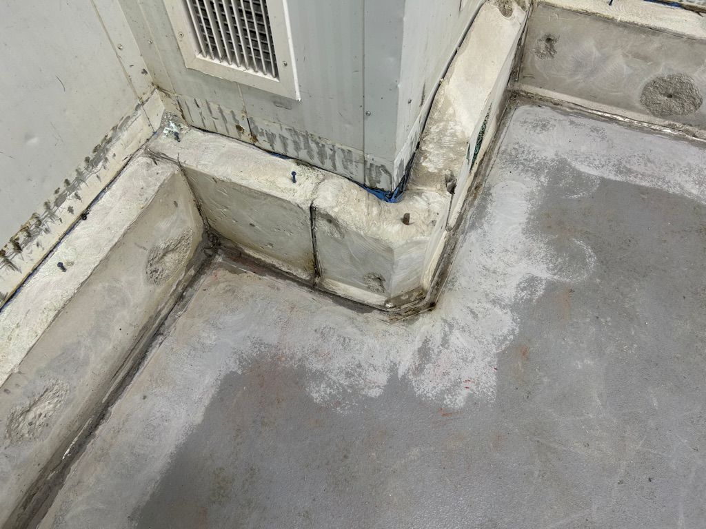 Concrete floor-to-wall corner with worn patches, anchoring screws and vent before polymer repair