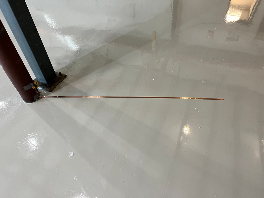 Smooth shiny white ESD floor with horizontal copper grounding strip and two vertical structural poles