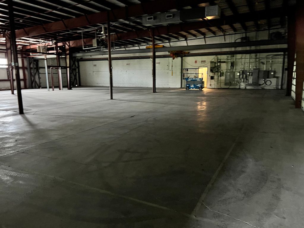 Large empty industrial warehouse with concrete floor, metal support columns and electrical panels, blue scissor lift near bright open doorway