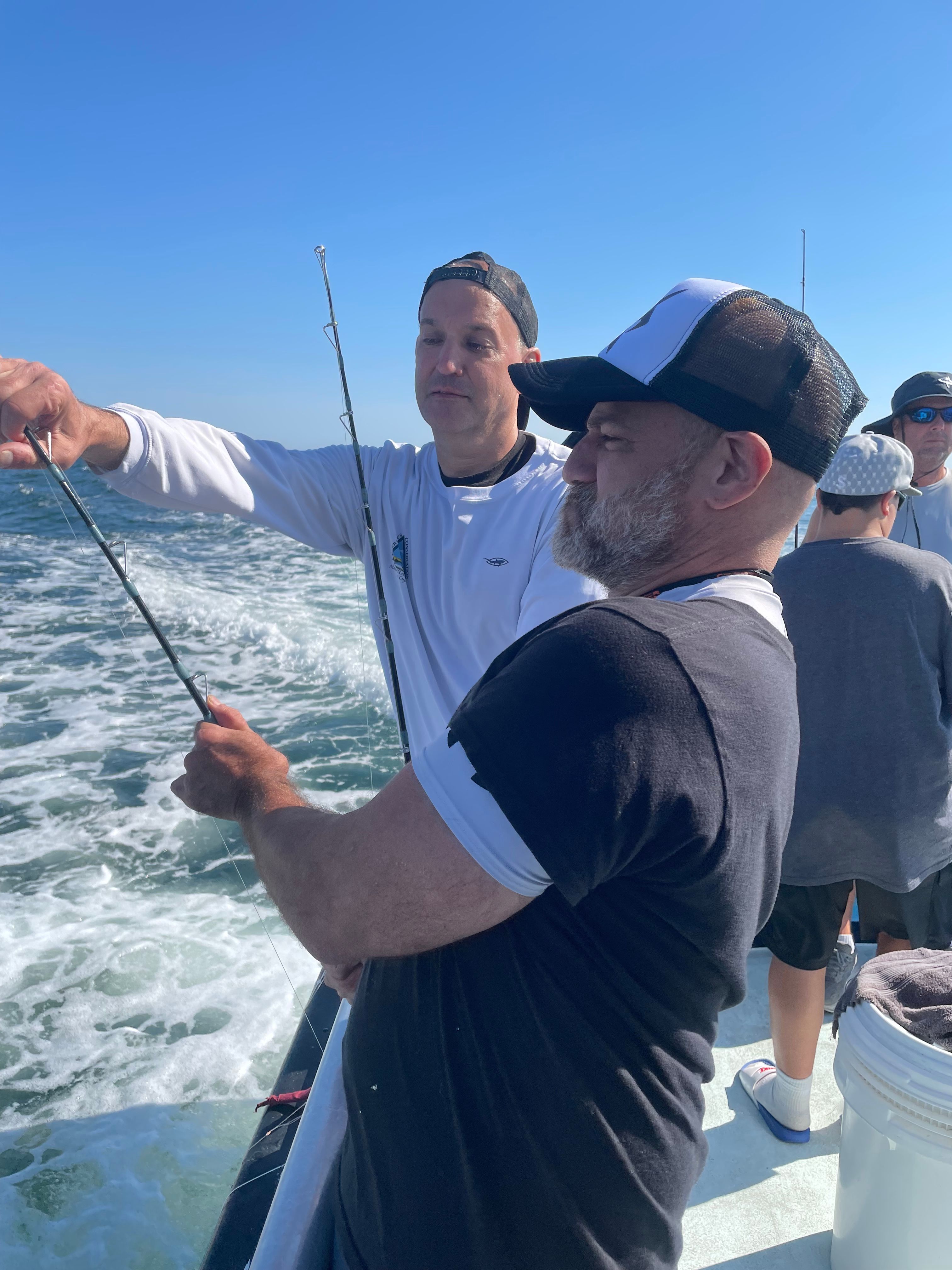 Four men on a fishing boat at Montauk, holding rods over the water, blue sky and distant shoreline