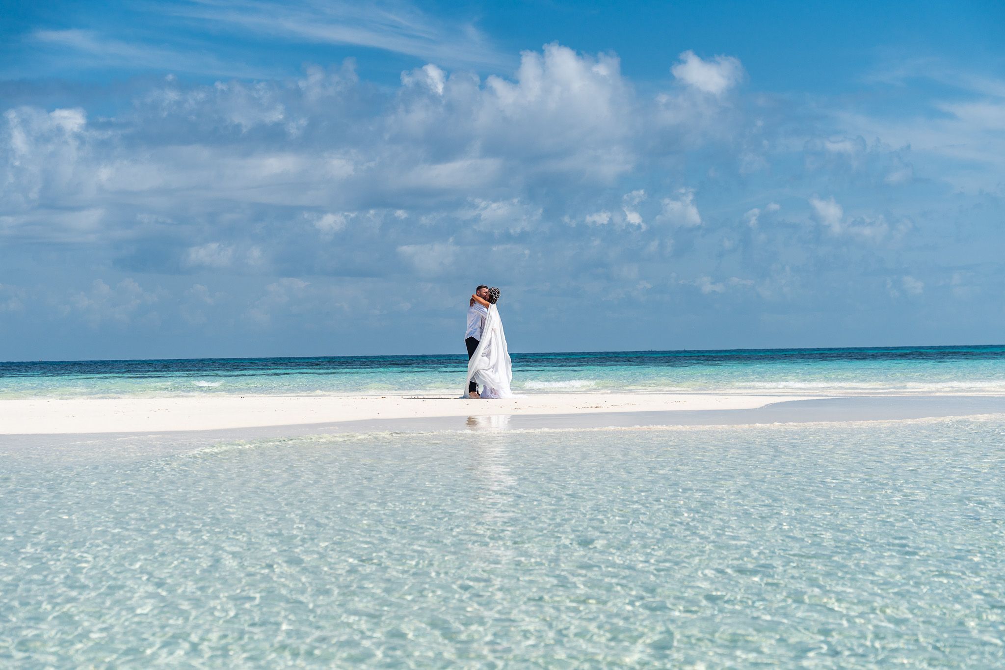 Couple on white sandbank beach in Zanzibar - crystal clear water