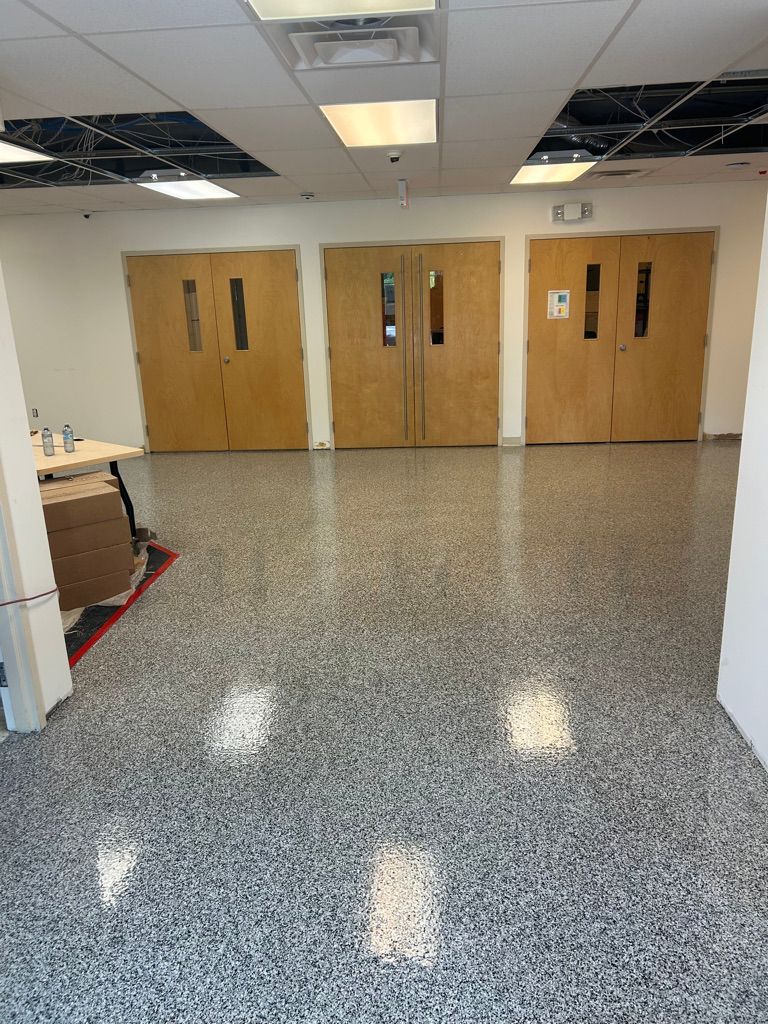 School common area with shiny speckled gray epoxy floor, three sets of wooden double doors and white ceiling tiles