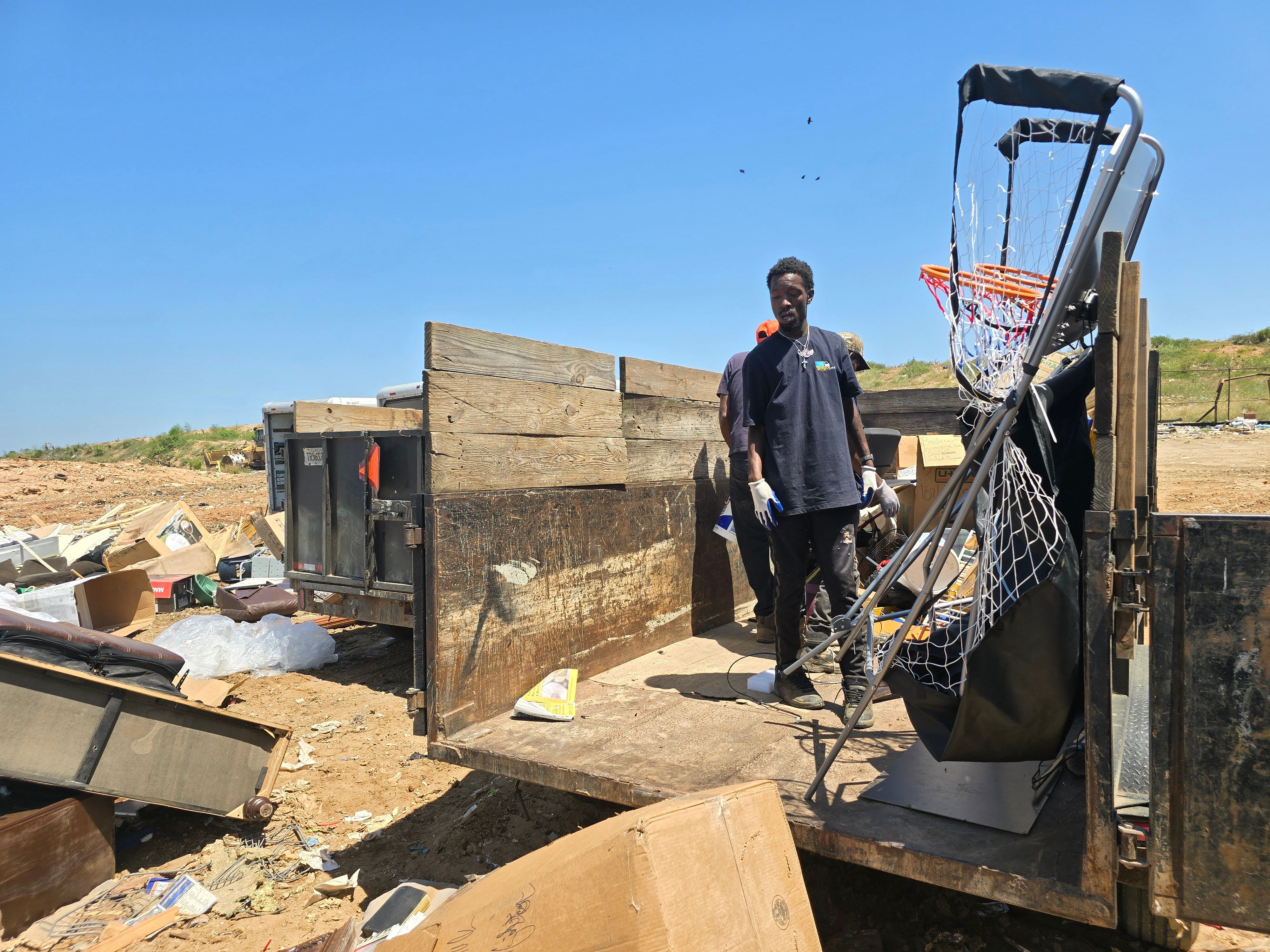 GoGo Junk Removal worker standing on loaded trailer with basketball hoop and discarded items