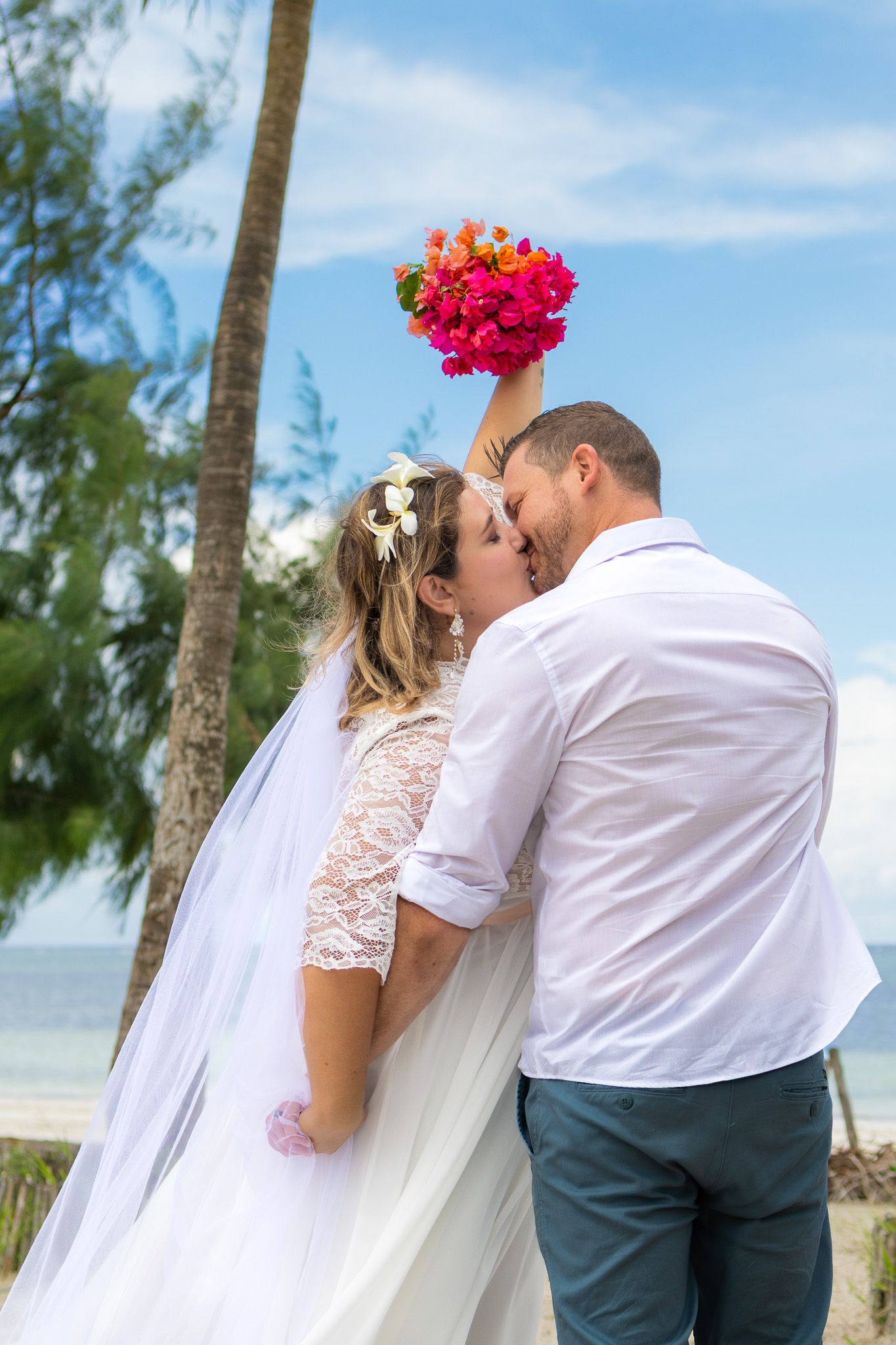 Couple kissing near palm tree with bouquet raised high