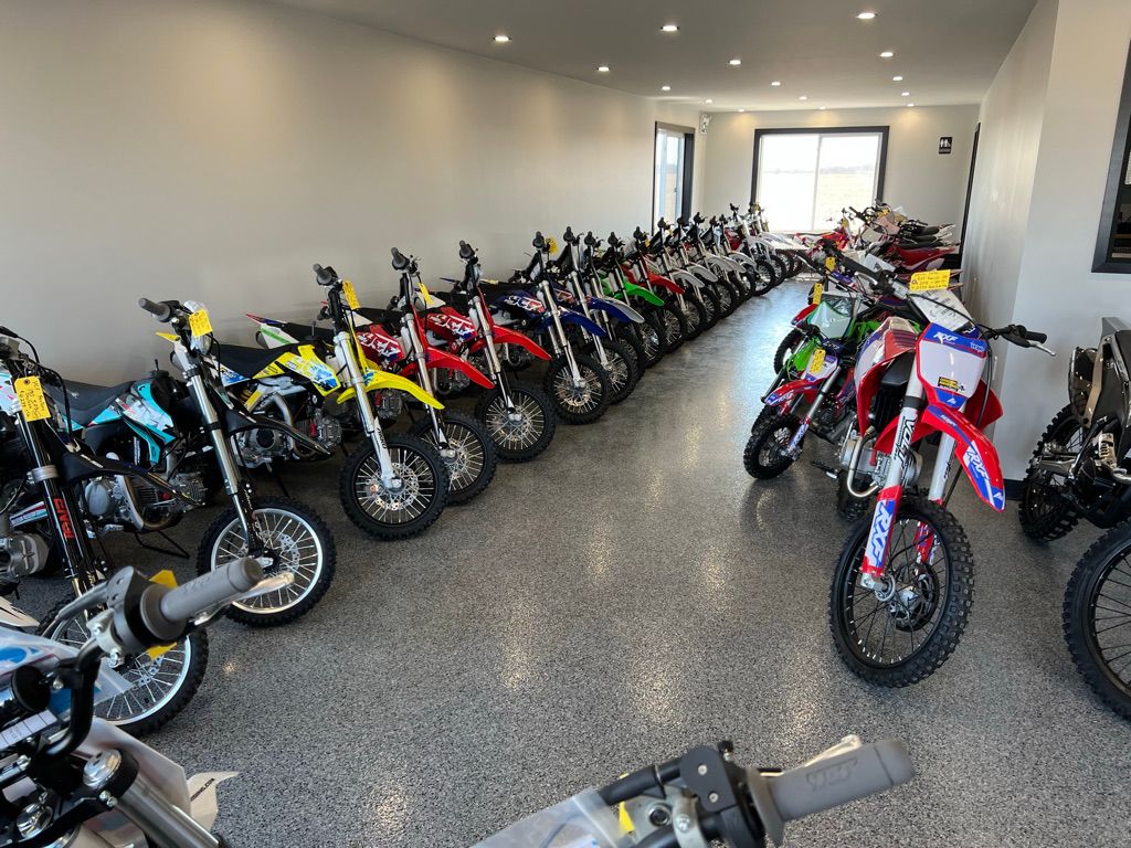 Retail showroom with polished floor and two parallel rows of colorful dirt bikes with yellow price tags under ceiling lights