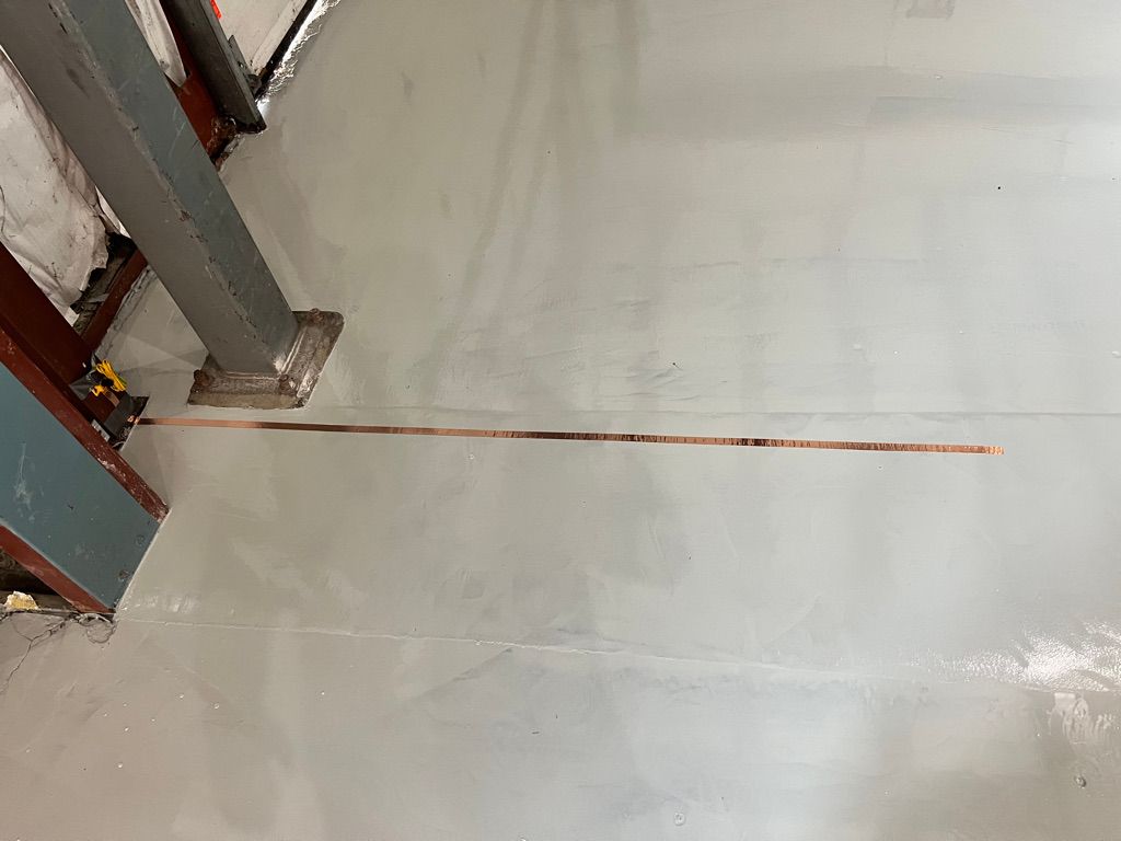 Gray concrete ESD floor with long copper grounding strip running parallel to vertical metal structural beams
