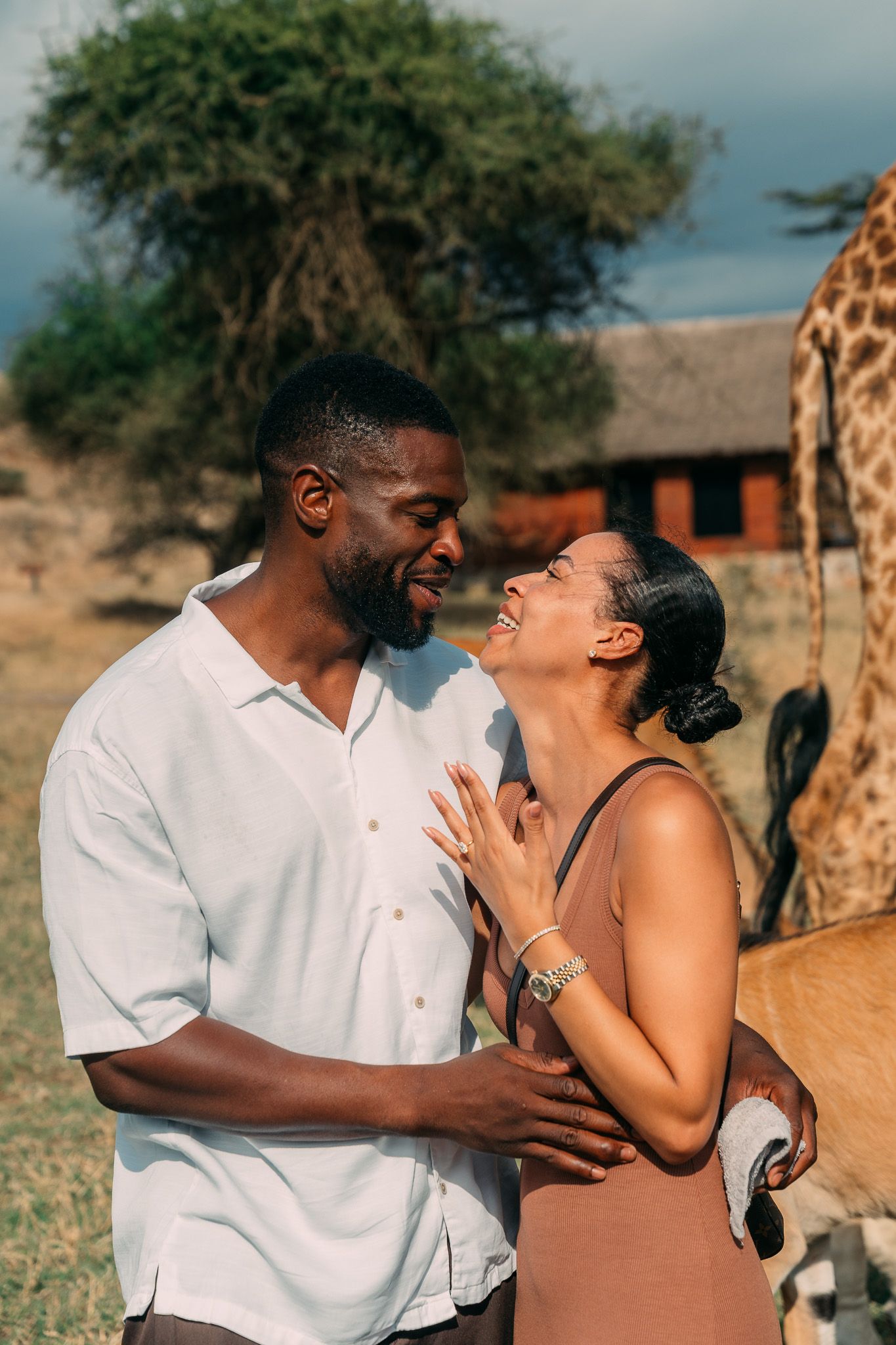 Couple smiling together with giraffe in background at Serval Wildlife Park