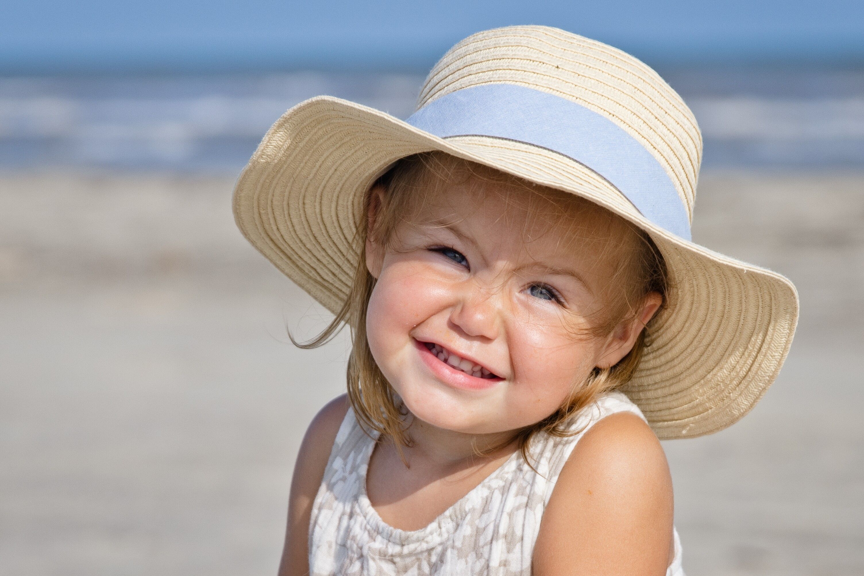 Little girl with a big straw hat, smiling on the beach