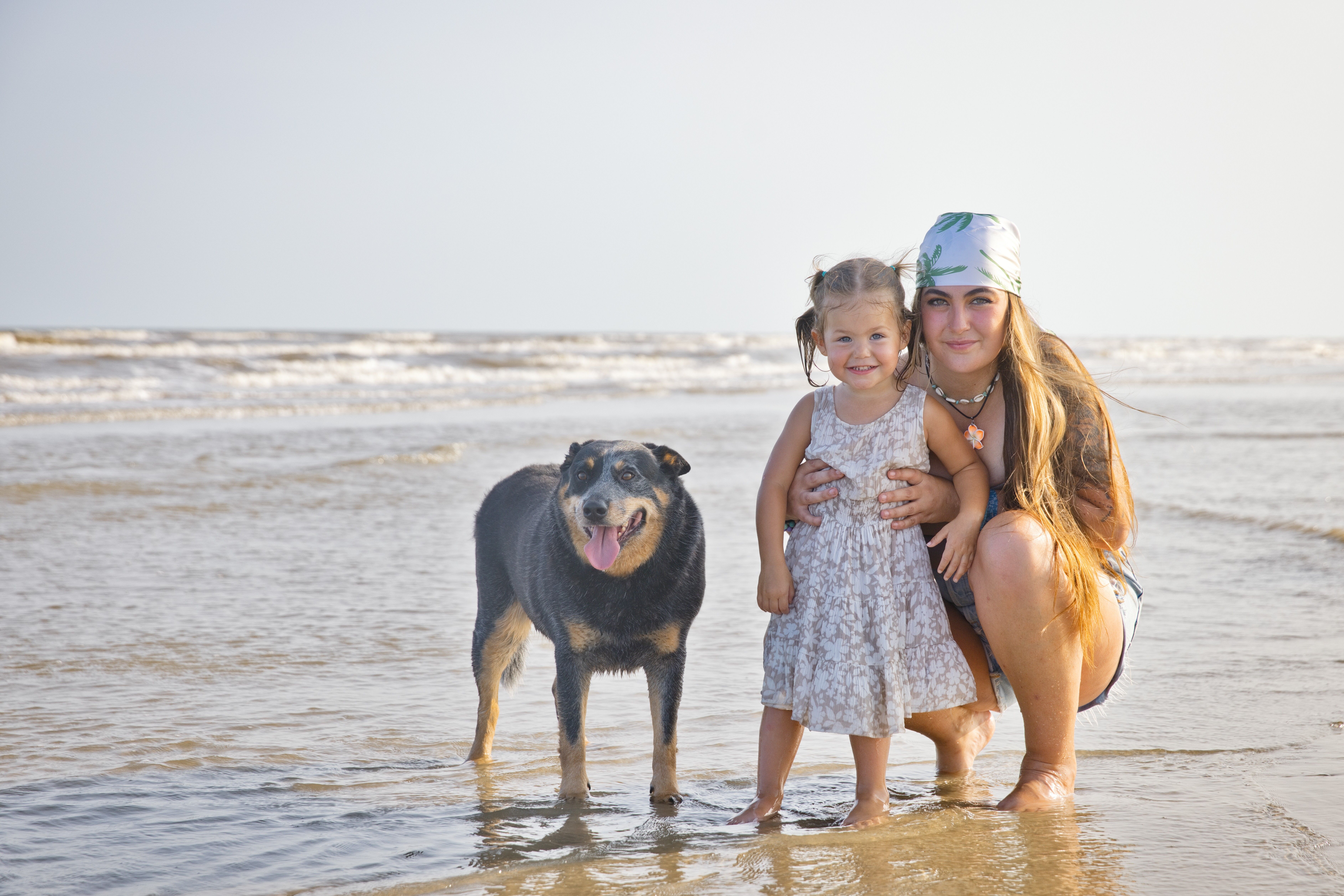 Mom crouching on the beach holding her little girl