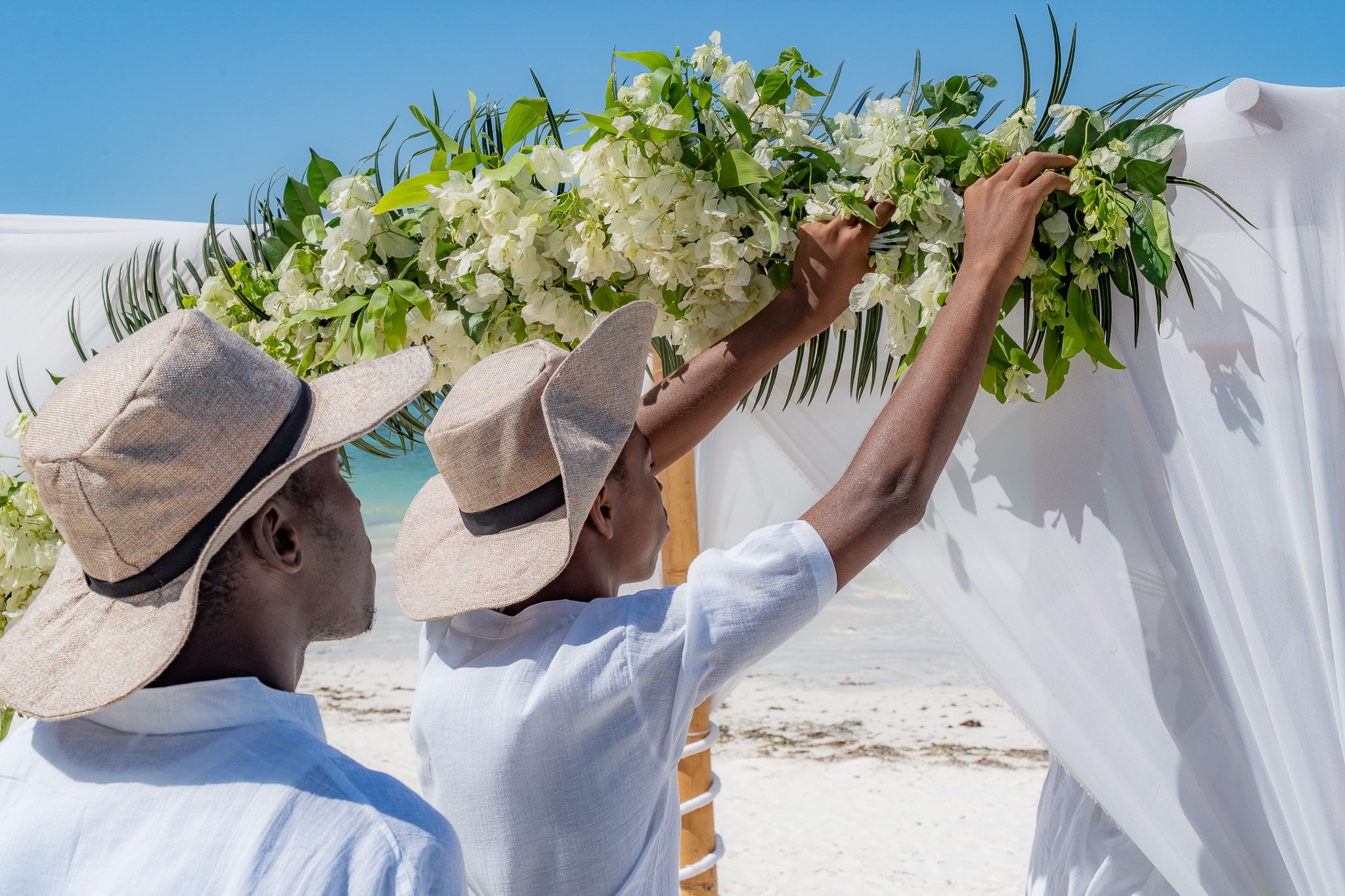 Team arranging fresh white flower garlands on beach canopy
