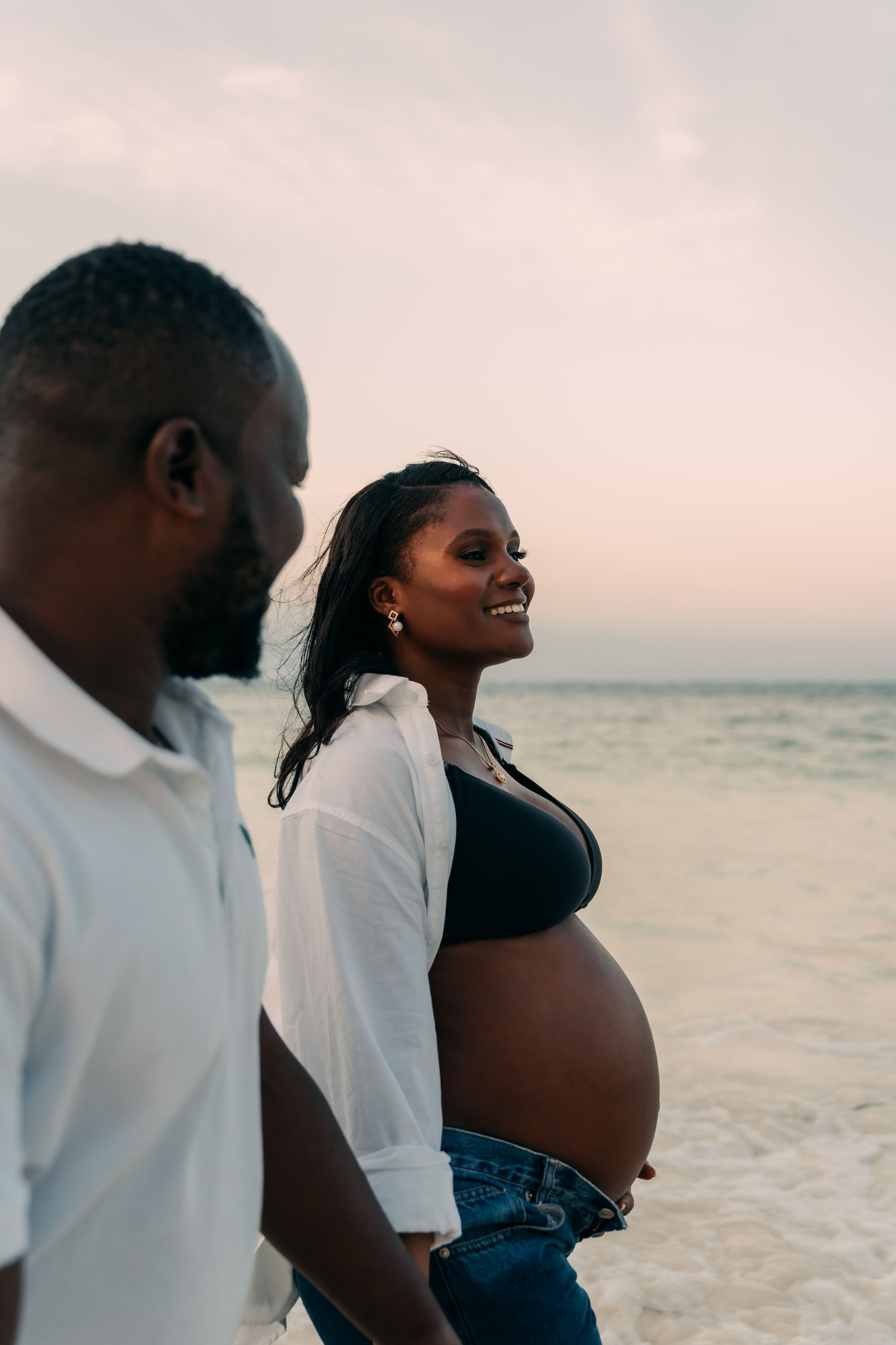 Pregnant woman and partner walking along Zanzibar beach at golden hour