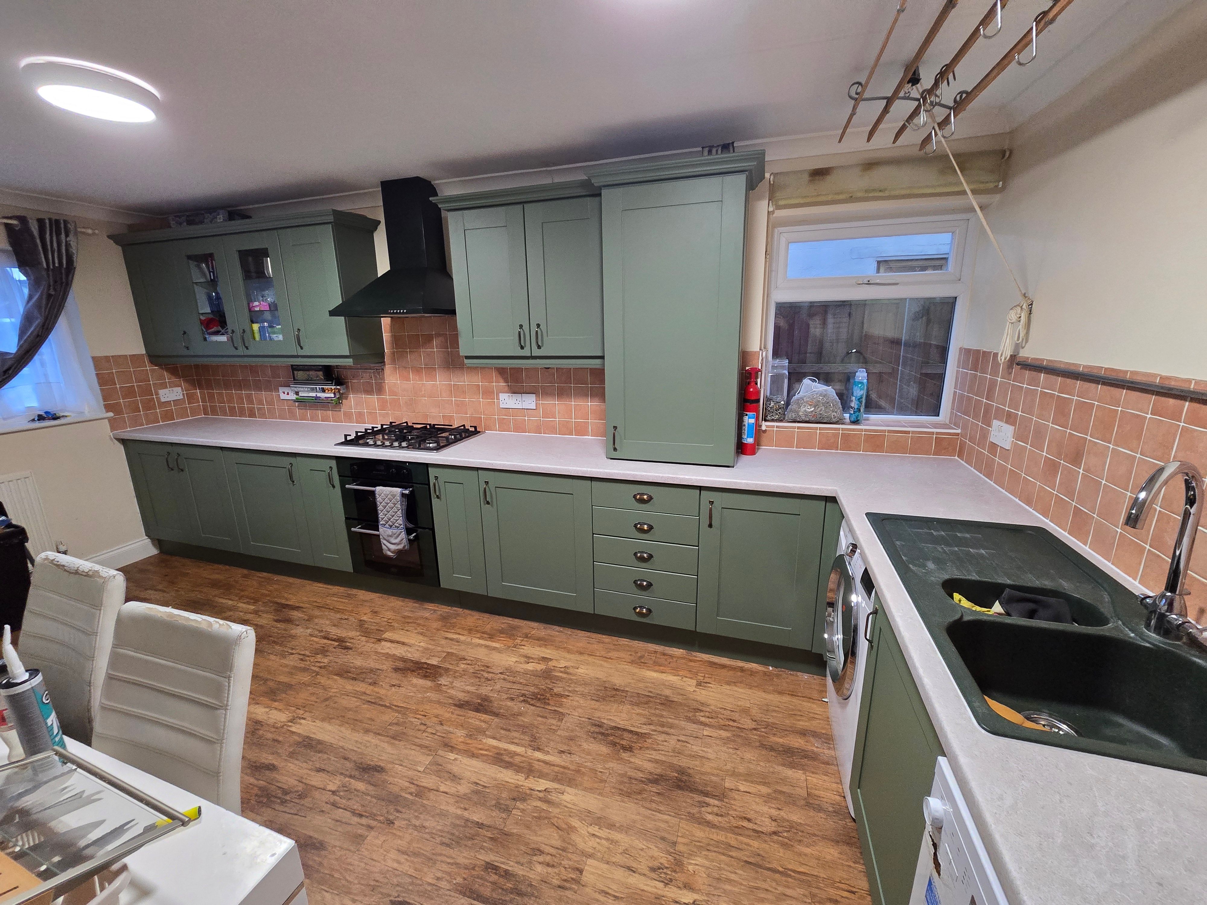 Kitchen after wrapping — wide shot showing full sage green kitchen with stone-effect worktops and black range hood