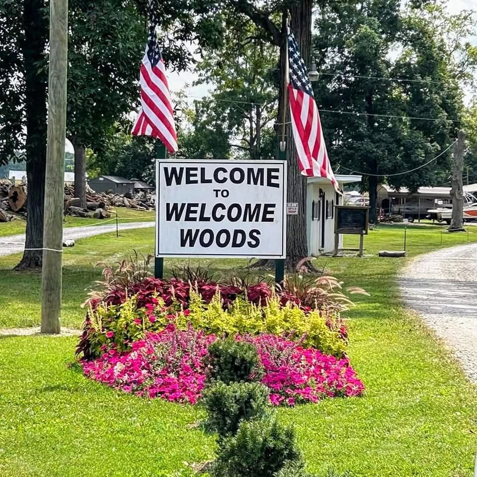 Welcome to Welcome Woods sign with American flags and flower bed