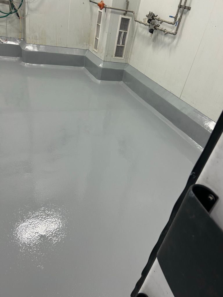 Clean manufacturing room with smooth shiny grey epoxy floor and matching grey seamless baseboards
