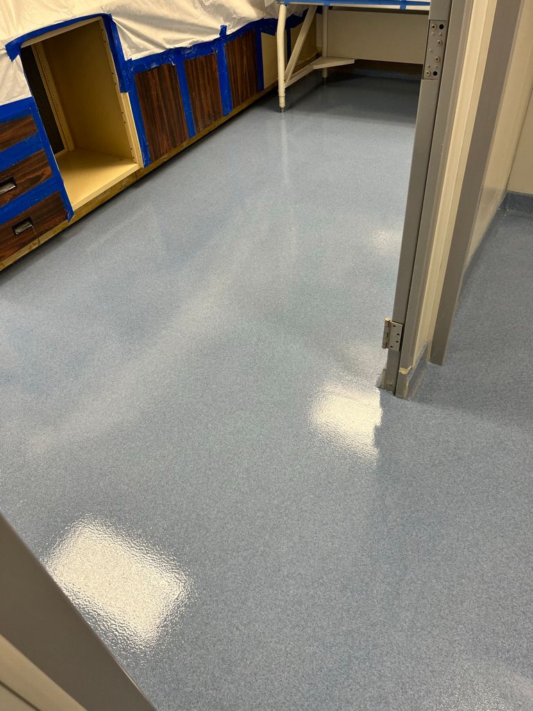 Newly installed light blue seamless floor in a pharmaceutical room with open cabinets taped off and countertop framing visible