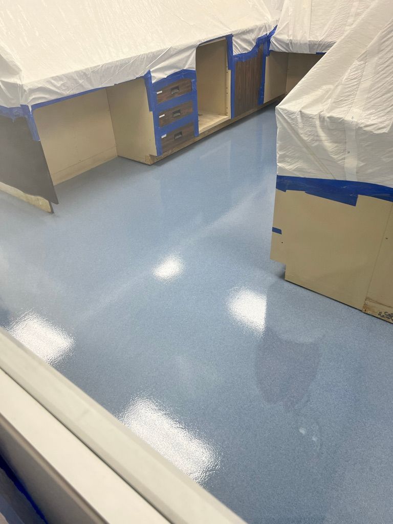 Pharmaceutical lab room with shiny light blue epoxy floor and cabinets wrapped in white protective sheets secured with painter's tape