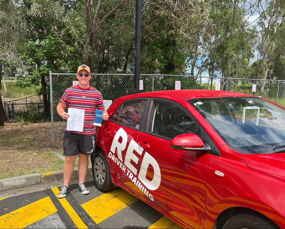 Confident new driver standing beside RED Driver Training car in Coomera after passing practical driving test