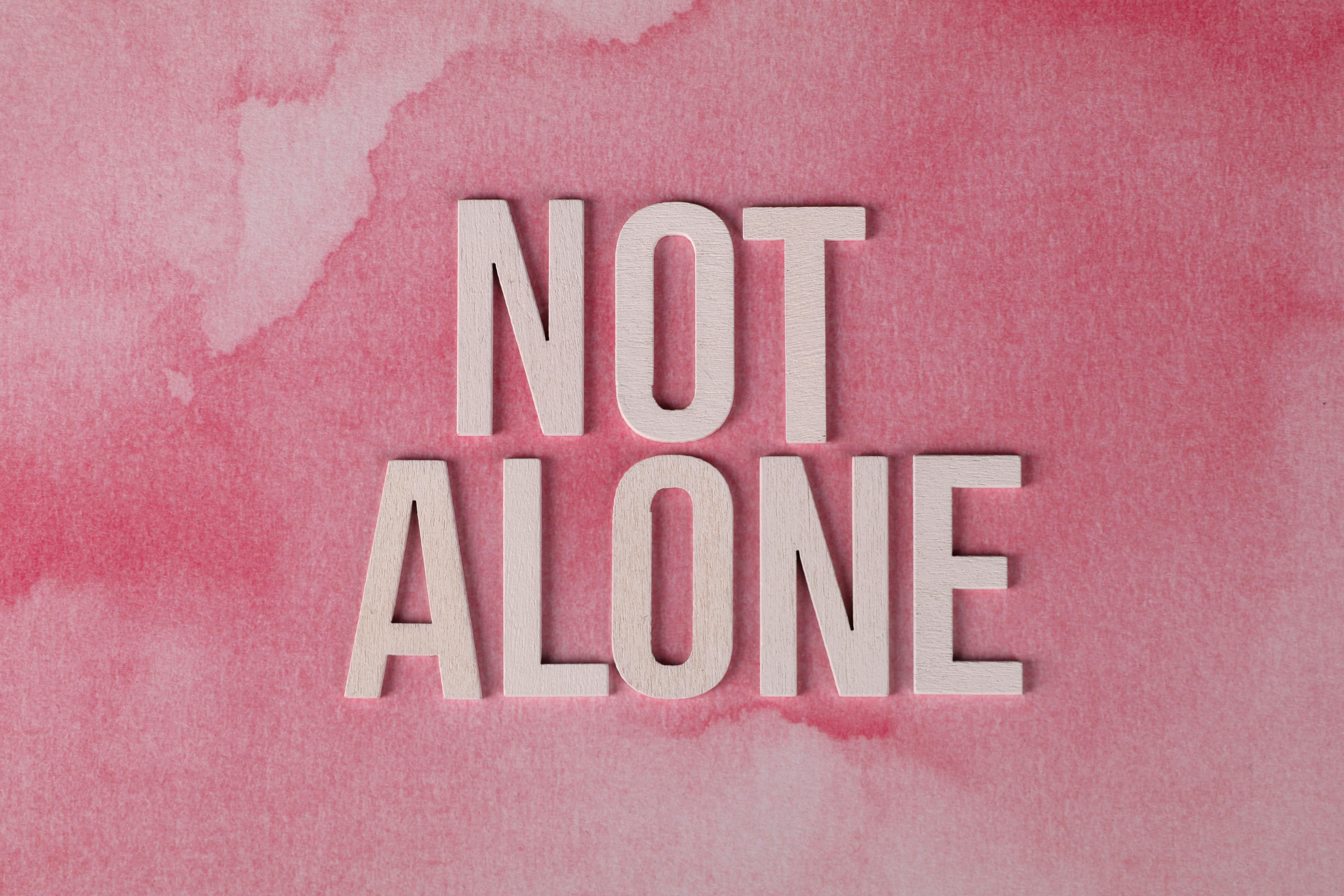 Wooden letters spelling NOT ALONE on a pink background