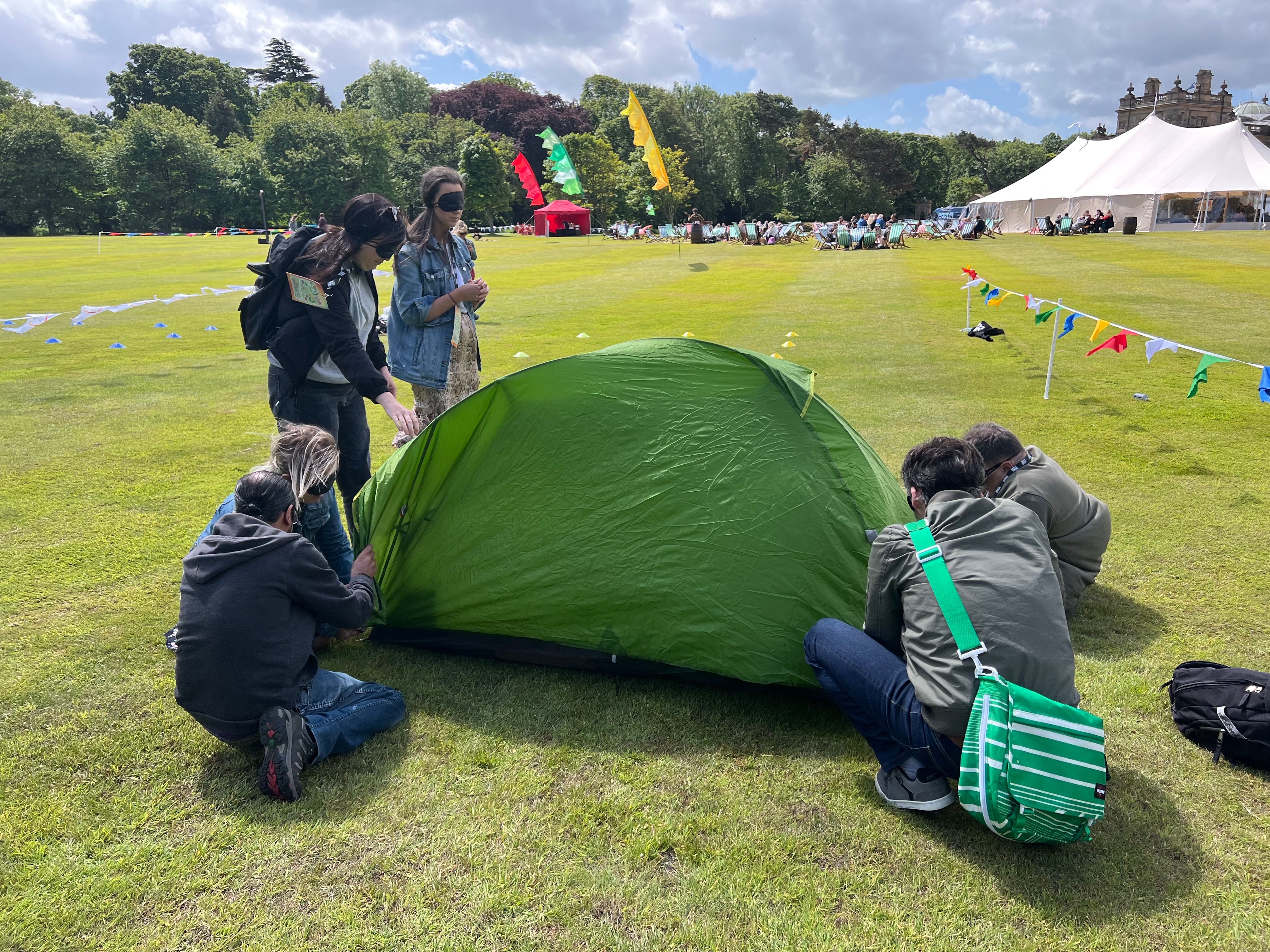 Take Me Back team building event — six participants working together around a green tent with blindfolds and bunting at an outdoor corporate event