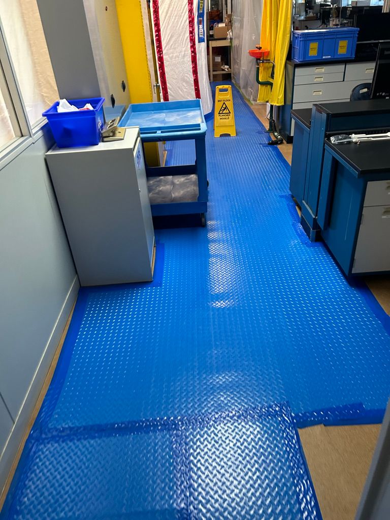 Pharmaceutical lab corridor with completed blue textured seamless floor, lab cabinetry, emergency eyewash station and wet floor signage in place