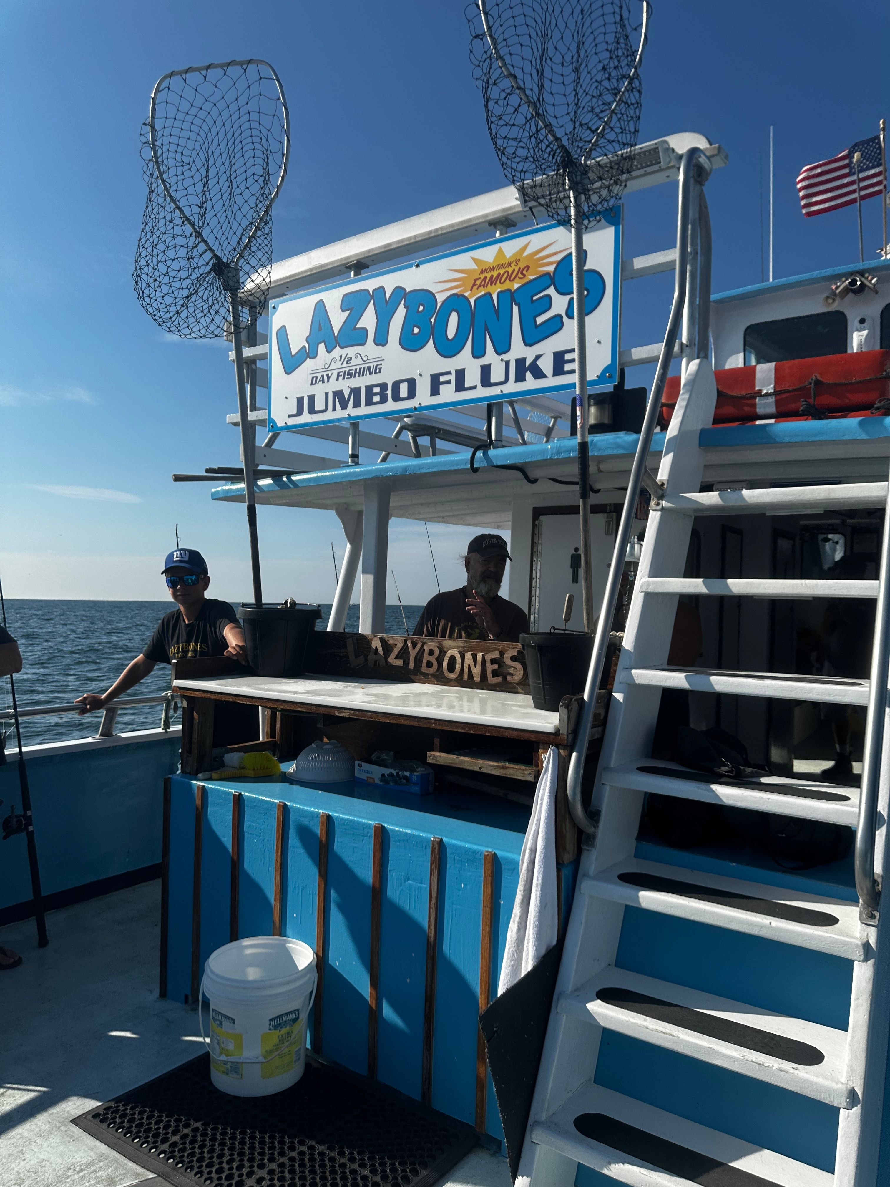 Lazybones fishing boat at Montauk marina, two men on deck, American flag, fishing nets on poles, sunny day