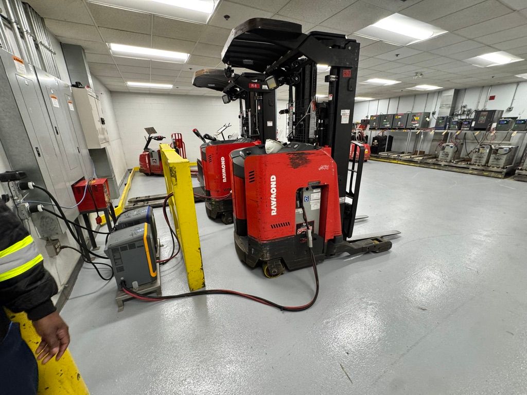Three red Raymond forklifts lined up at charging stations on smooth grey epoxy floor in manufacturing facility