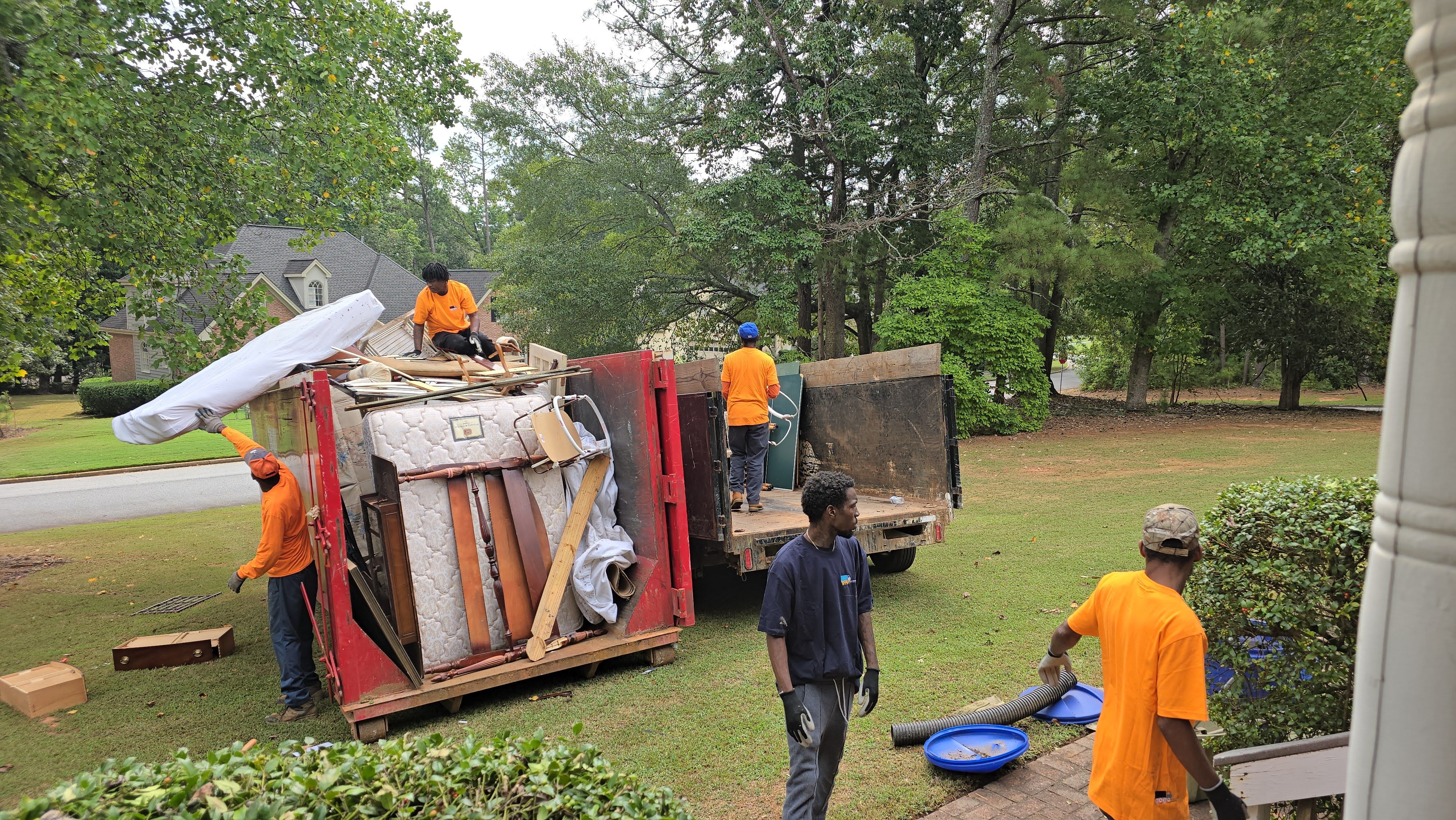 GoGo Junk Removal team loading mattresses and debris into red dumpster at residential property